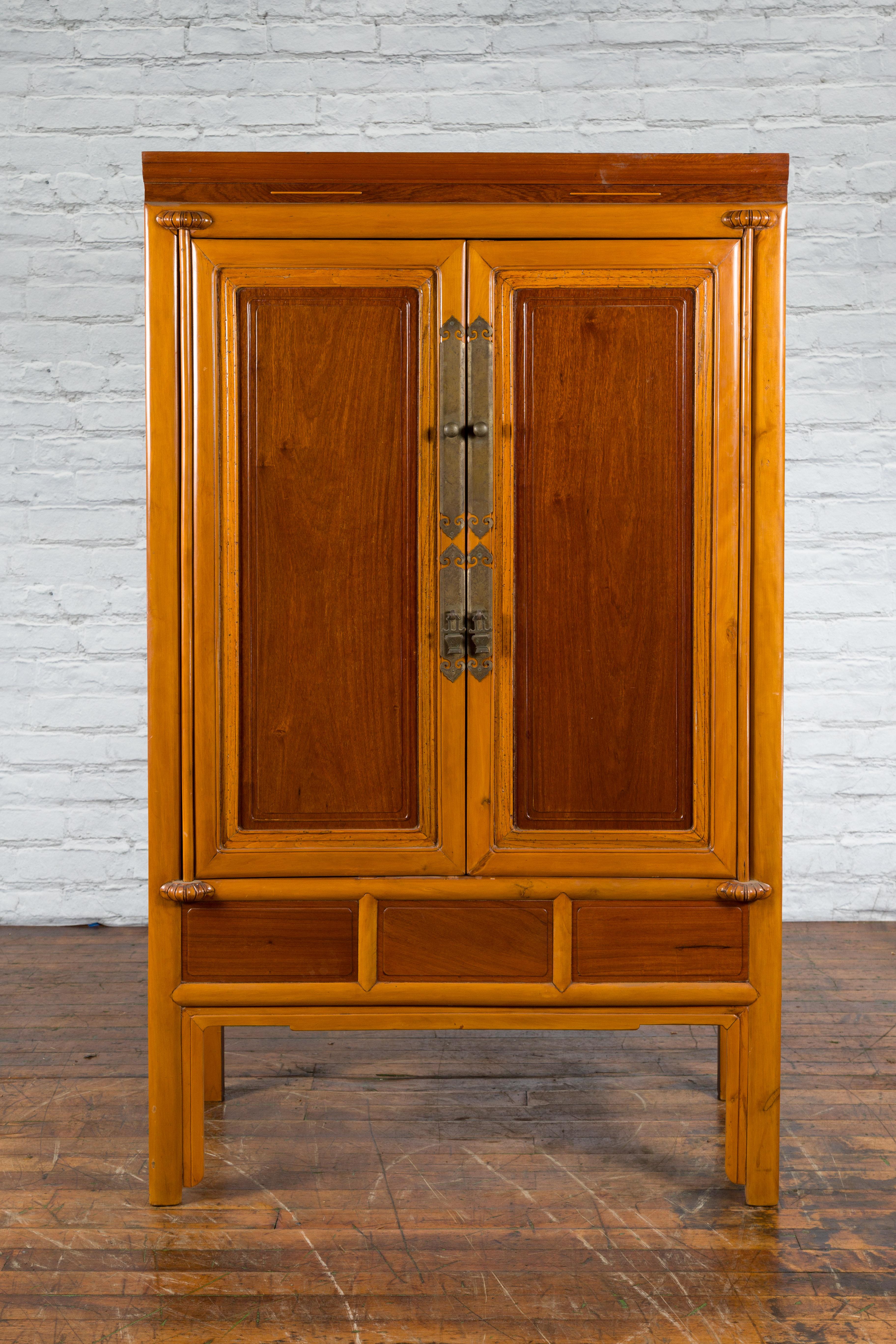A Chinese Qing Dynasty period two-toned wooden cabinet from the 19th century, with brass hardware. Created in China during the Qing Dynasty in the 19th century, this tall cabinet features a linear silhouette perfectly complimented by a two-toned