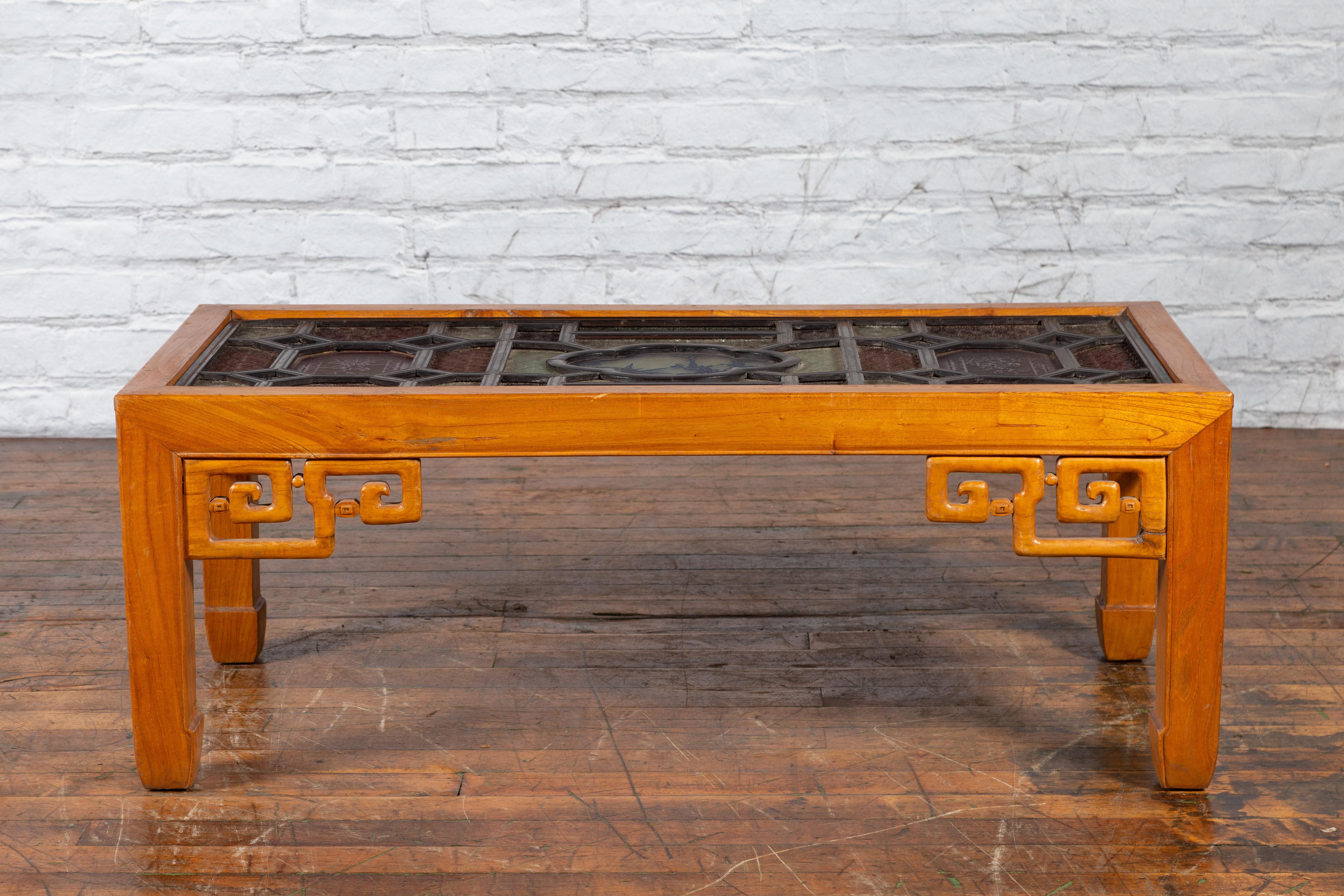 A Chinese Qing Dynasty period wooden coffee table from the 19th century with stained glass top and openwork motifs. Created in China during the Qing Dynasty, this coffee table features a rectangular top adorned with multicolored embossed stained