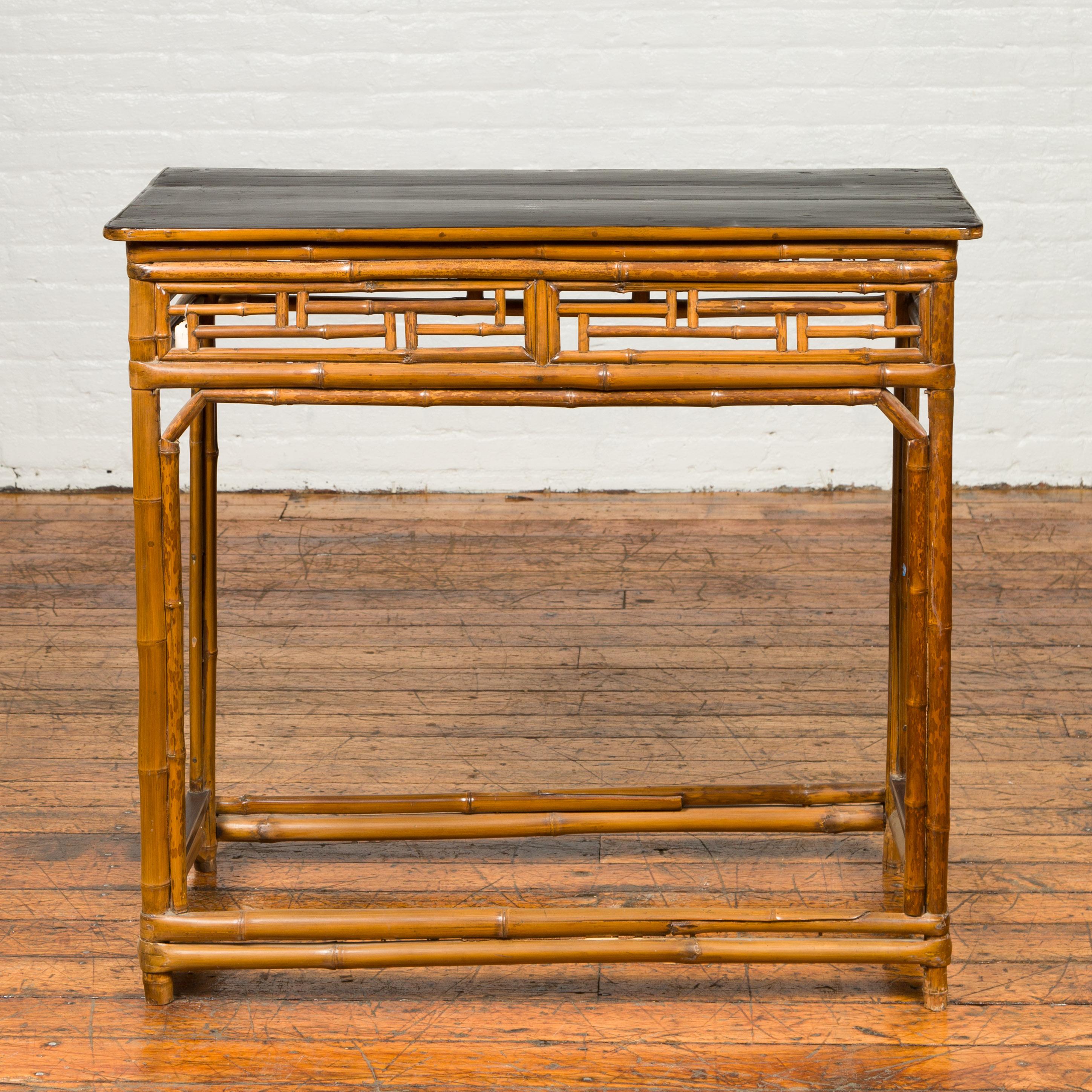 A Chinese Qing dynasty bamboo altar console table from the 19th century, with black lacquered top and geometric motifs. Born in China during the 19th century, this altar table features a black lacquered rectangular top sitting above a bamboo base