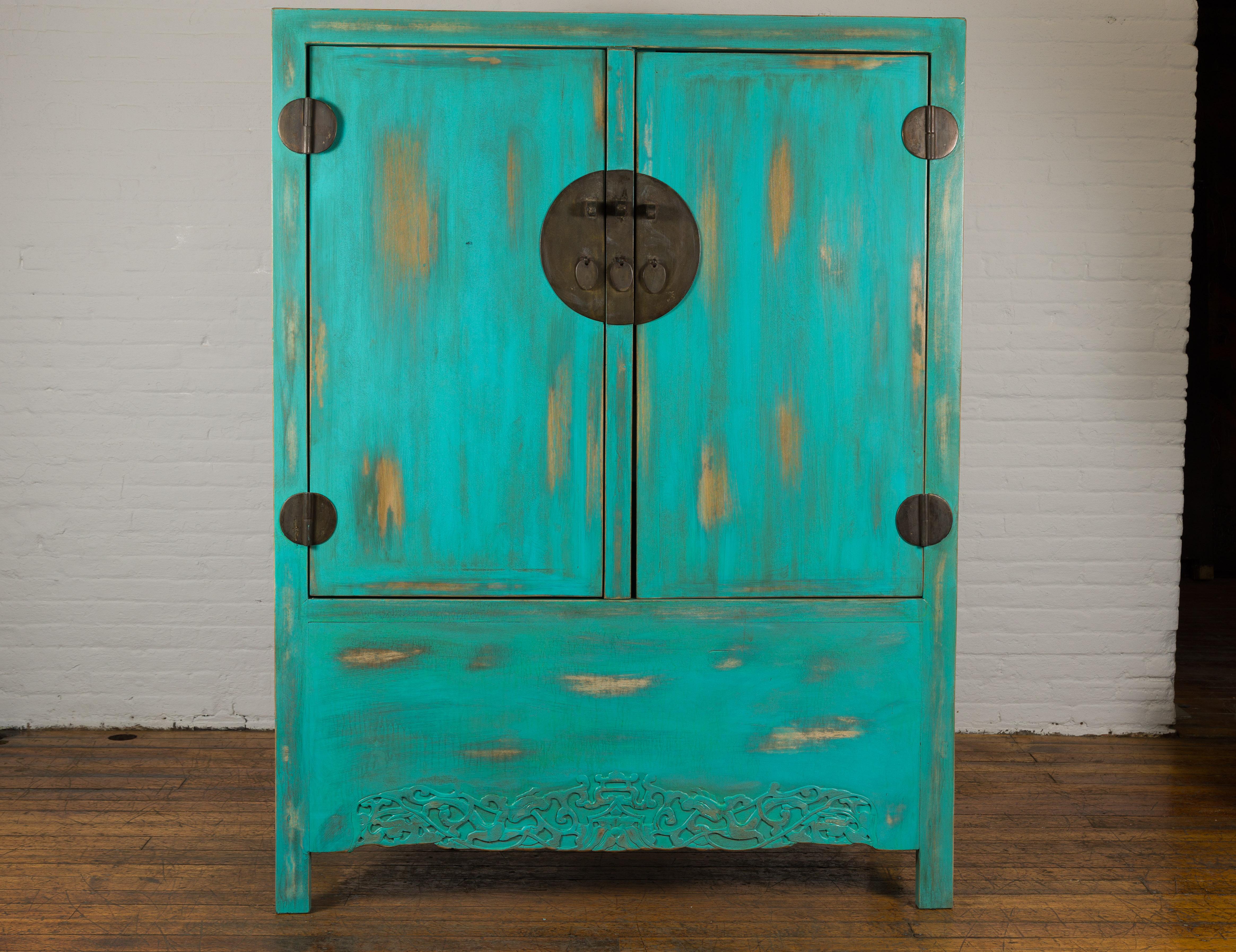 A Chinese Qing Dynasty period cabinet from the 19th century with custom distressed blue green lacquer, carved apron and brass hardware. Immerse yourself in the opulence of ancient China with this Qing Dynasty period cabinet, a splendid marriage of