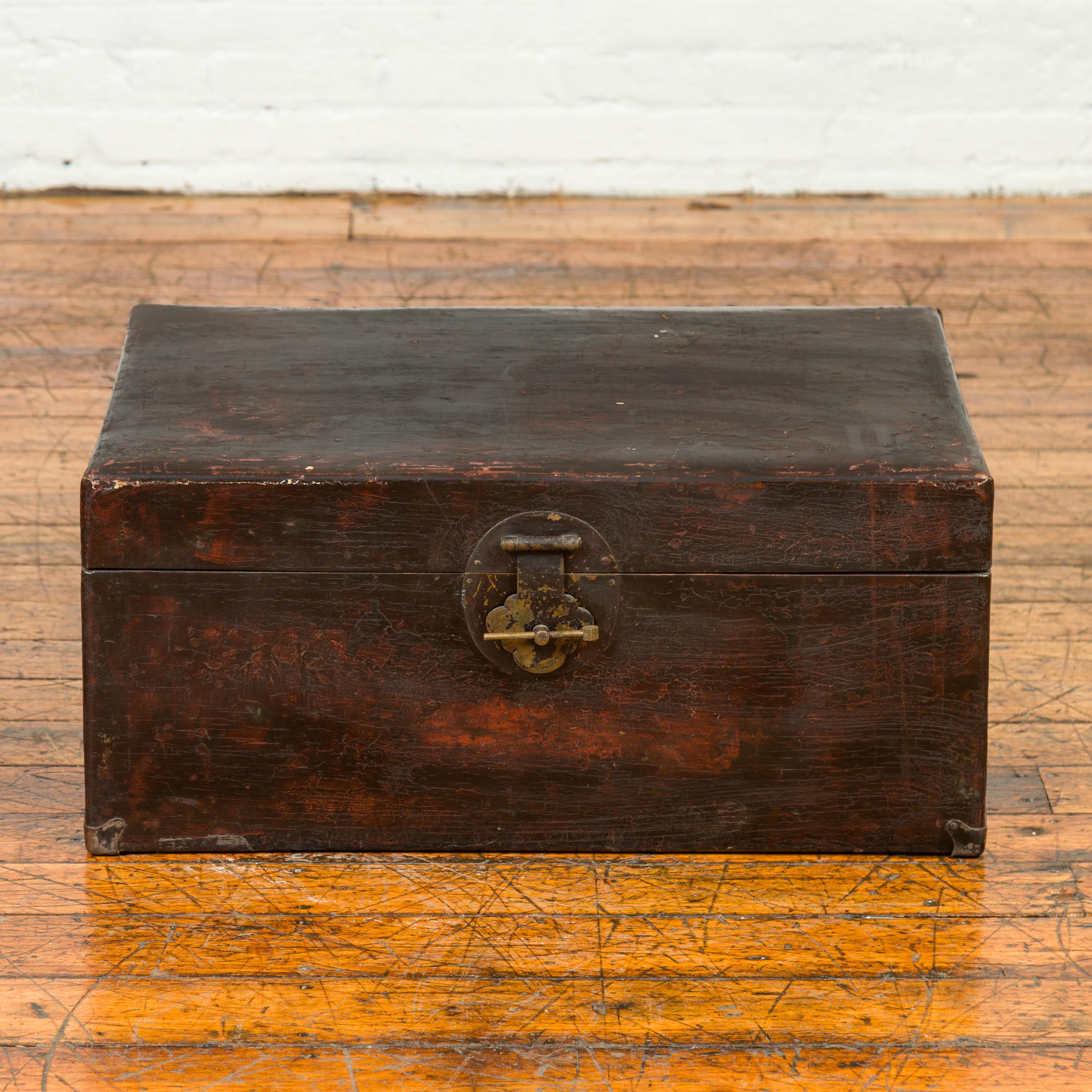 A Qing dynasty camphor wood blanket chest from the 19th century, with dark distressed patina and brass hardware. Immerse yourself in the rich history and timeless beauty of this Qing Dynasty camphor wood blanket chest from the 19th century. This