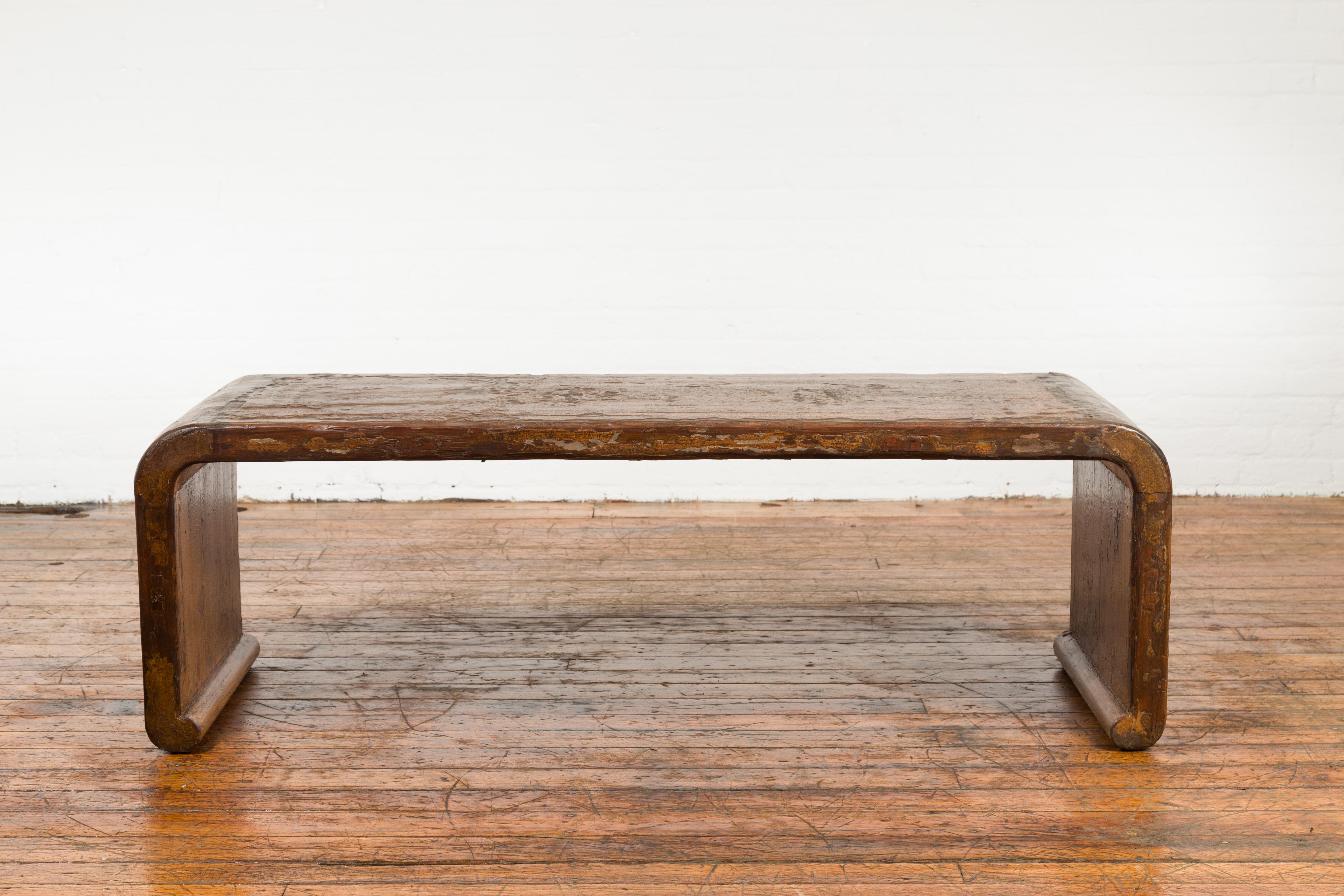 A Chinese Qing Dynasty period wooden waterfall coffee table from the 19th century, with distressed patina. Created in China during the 19th century this coffee table features a waterfall wooden frame with solid boards, boasting a nicely distressed