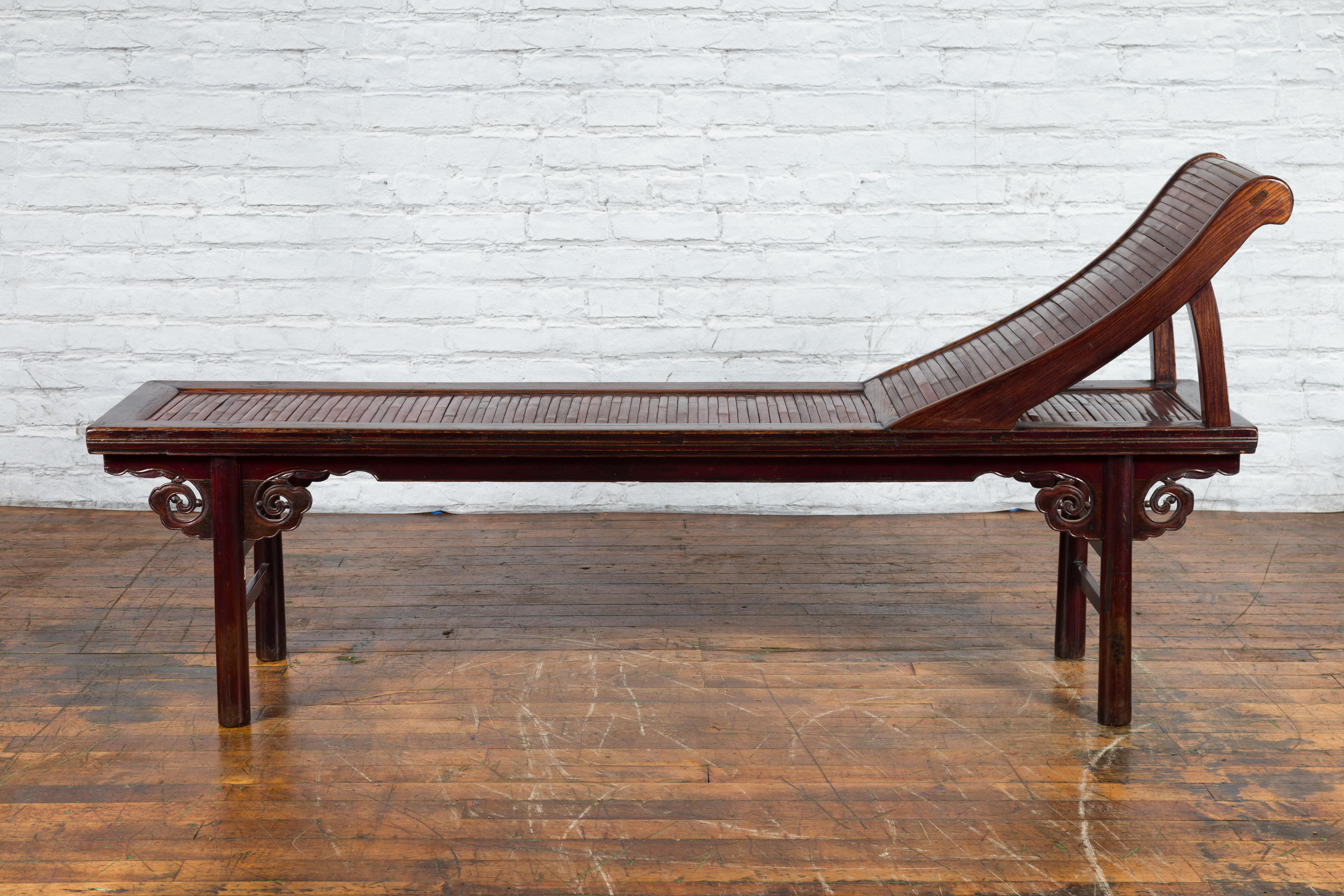 A Chinese Qing Dynasty period elm wood reclining lounge chair from the 19th century with bamboo slats and cloud-themed carved spandrels. Created in China during the Qing Dynasty in the 19th century, this elm wood lounge chair features a reddish