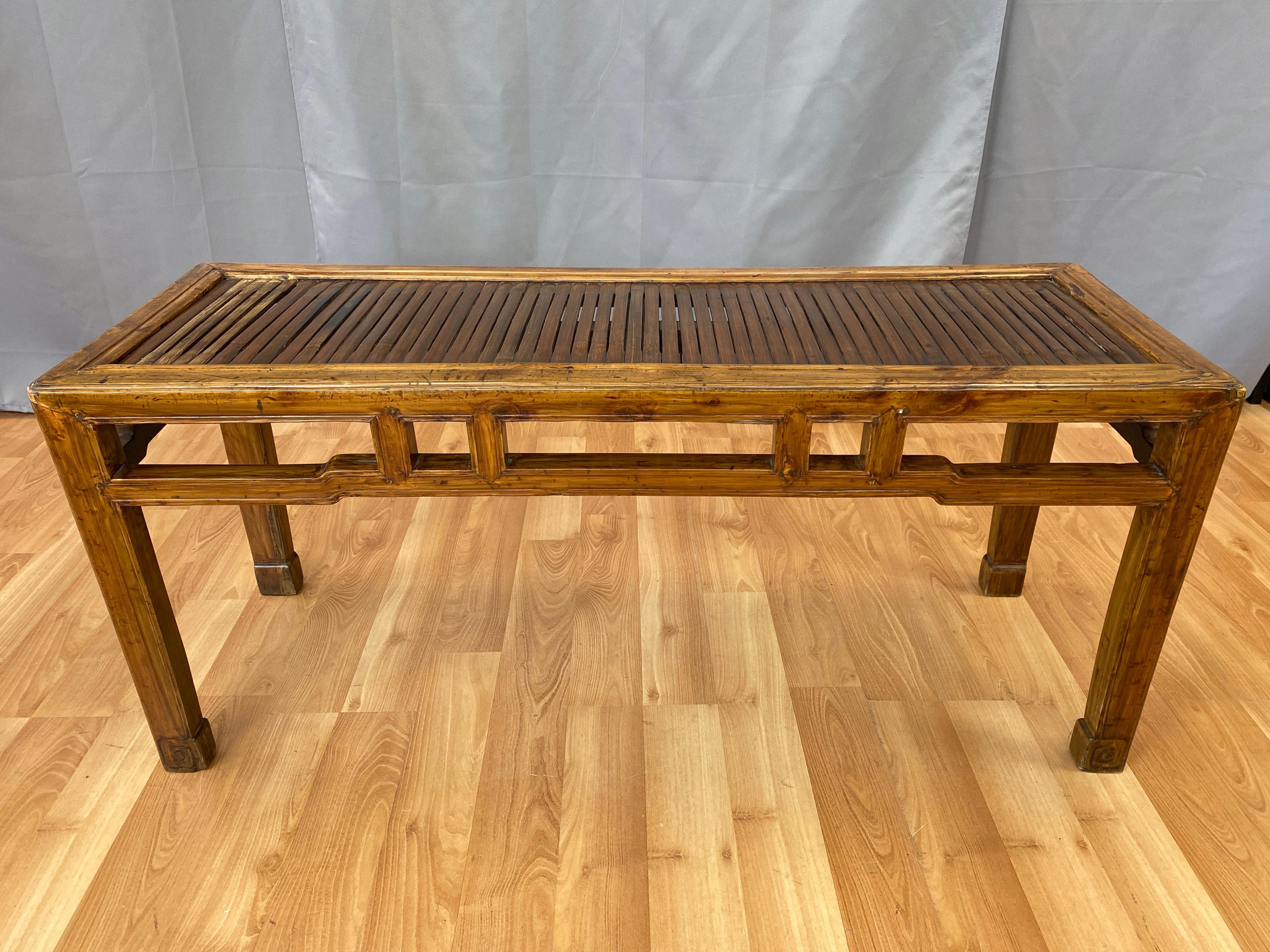 A 19th century later Qing dynasty period Chinese elm bench or coffee table with bamboo slat top.

Beijing form retains elements of its Ming era influence, including a lattice apron with sculpted trim and inward facing feet with carved coil detail on