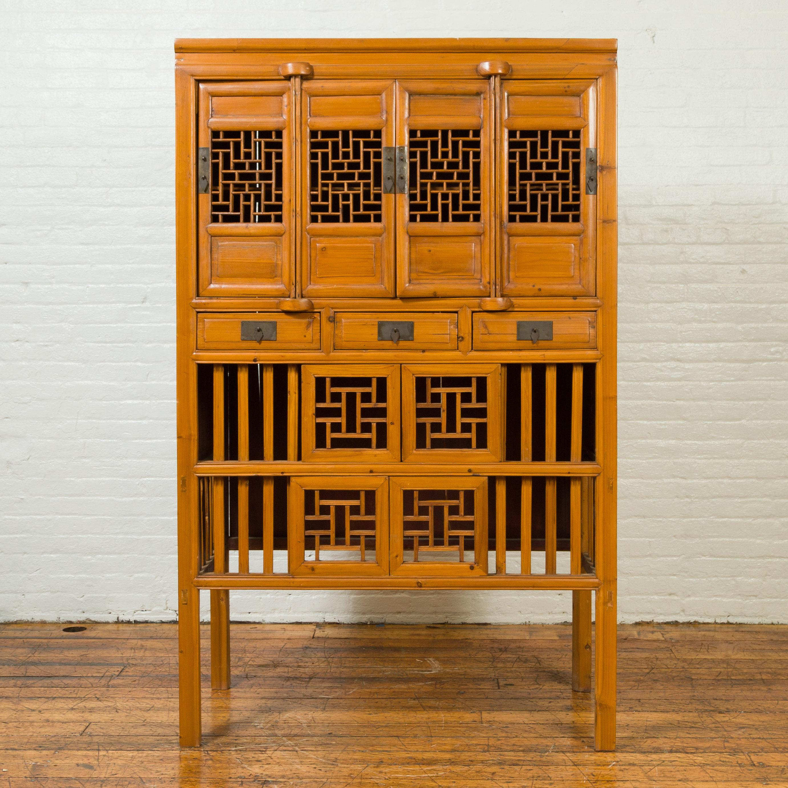 A Chinese Qing dynasty elmwood kitchen cabinet from the early 20th century, with fretwork and sliding doors. Born in China during the early years of the 20th century, this elmwood cabinet features four doors, each adorned with fretwork motifs and