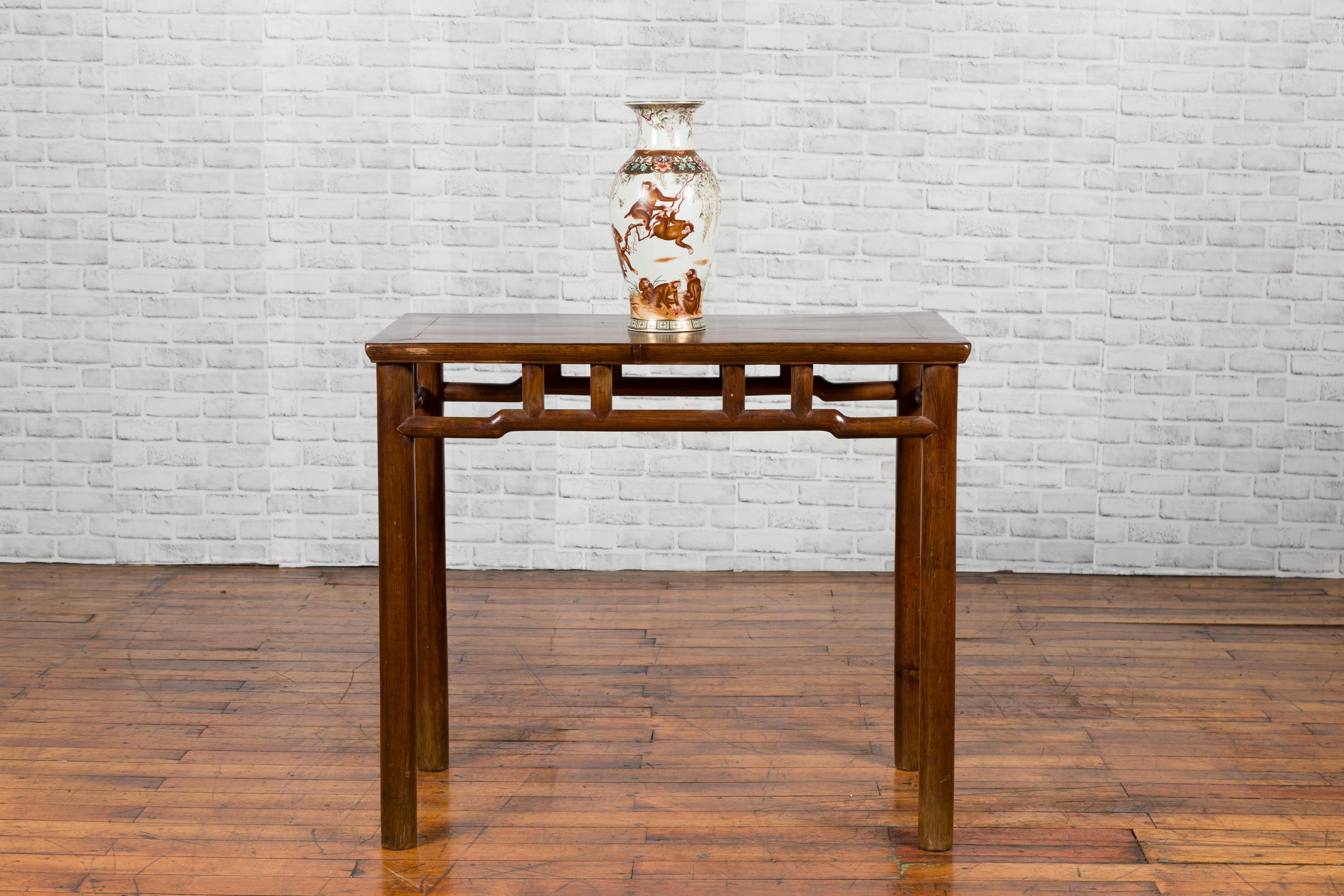A Chinese Qing dynasty period elm console table from the 19th century, with pillar strut motifs and humpbacked apron. Created in China during the Qing dynasty, this Chinese console table features a rectangular top with central board, sitting above a