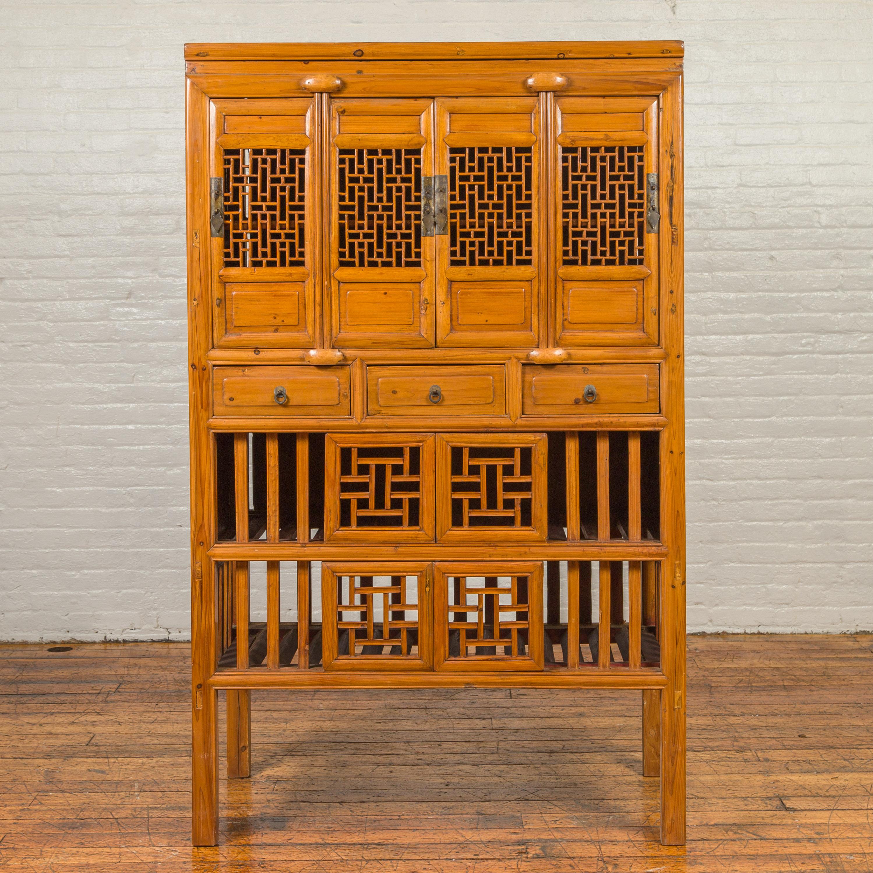A Chinese Qing dynasty period elmwood kitchen cabinet from the 19th century, with fretwork motifs, doors and sliding panels. Born in China during the 19th century, this elm cabinet features four doors, each adorned with fretwork motifs and opening