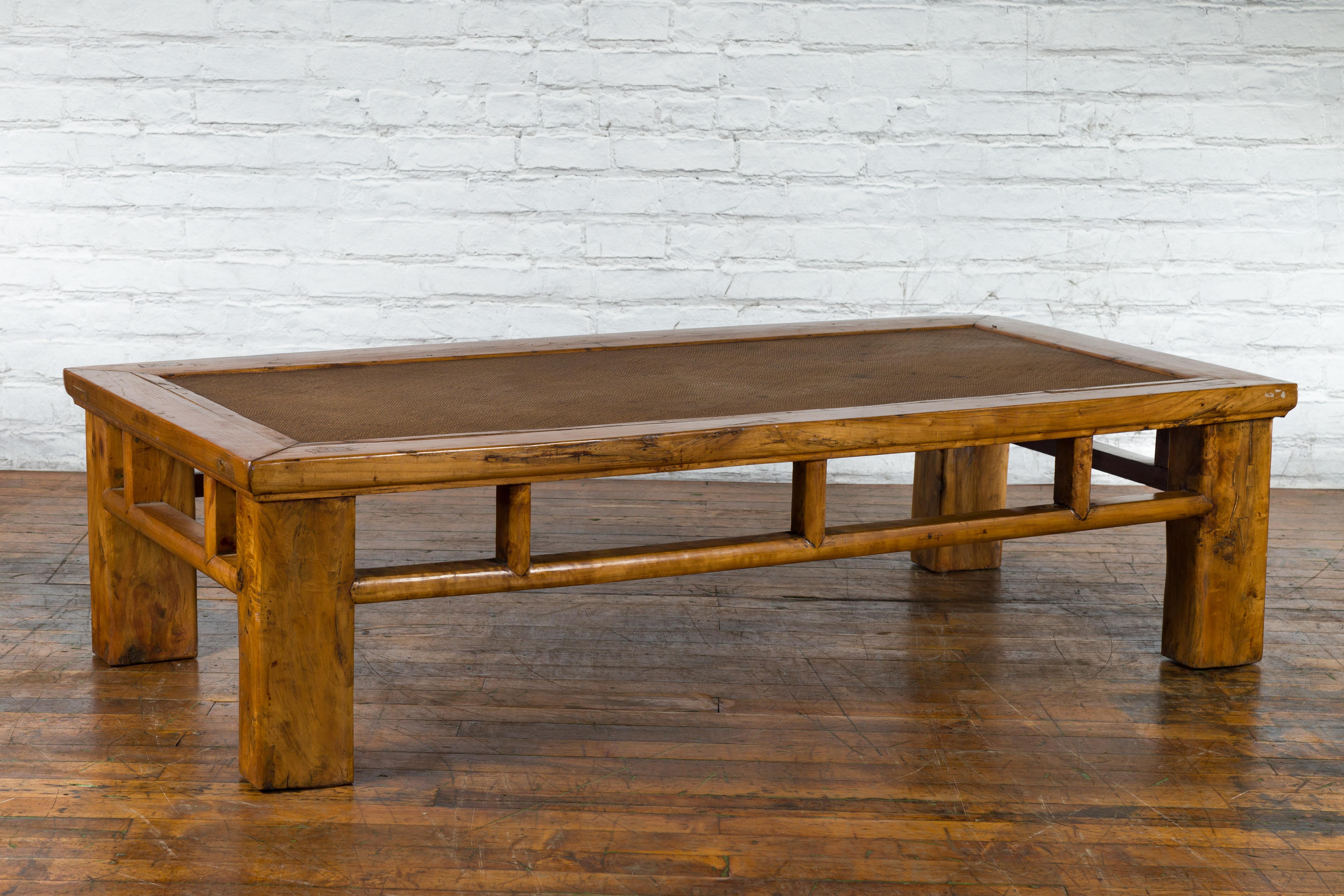 An antique Chinese Qing Dynasty period elm wood coffee table from the early 20th century, with hand-woven rattan top inset, square legs, open apron and pillar strut motifs. Created in China during the late Qing Dynasty period, this coffee table was