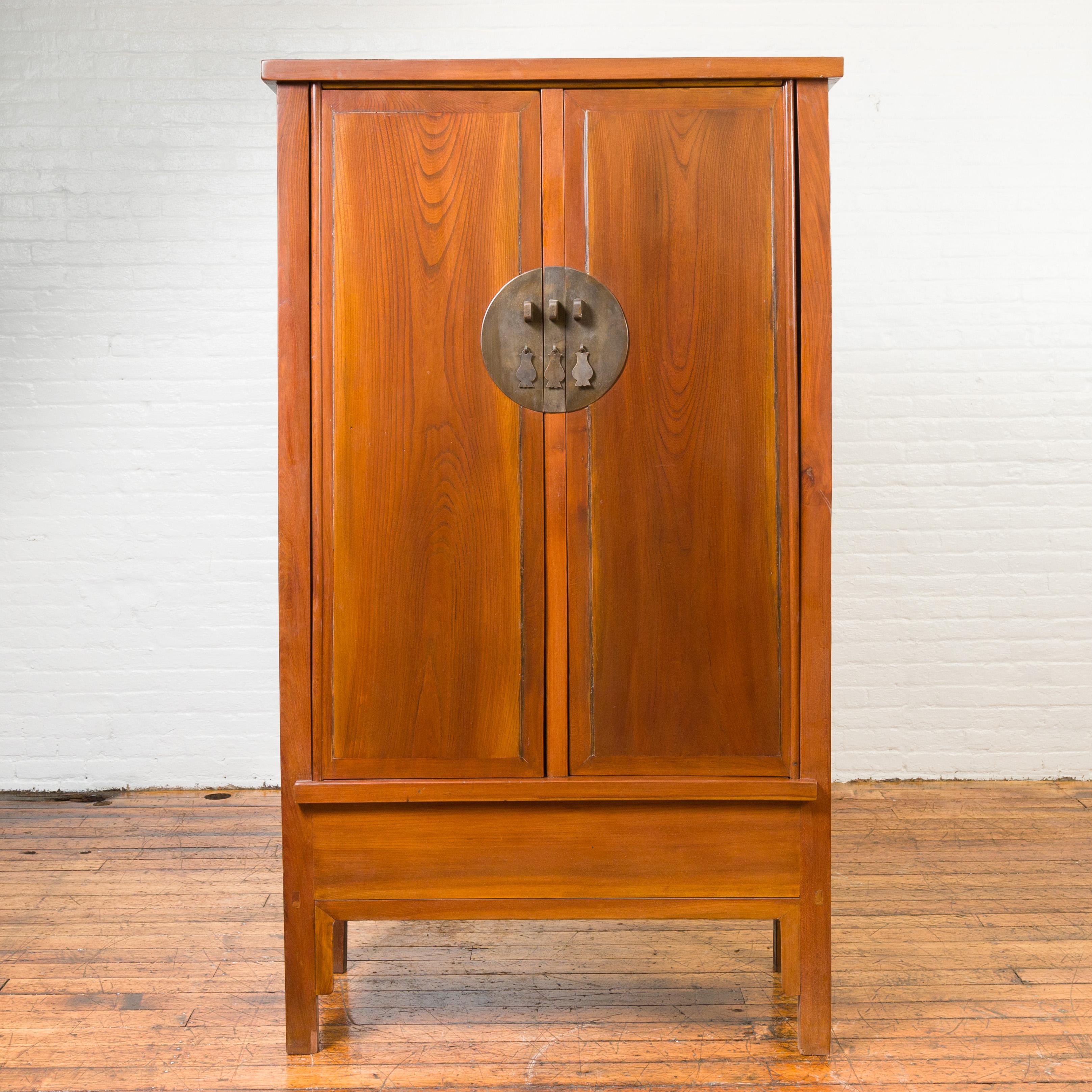 A Chinese Qing Dynasty elmwood cabinet from the 19th century, with bronze medallion hardware and inner drawers. Crafted in China during the Qing Dynasty, this elm cabinet features two large doors marked in their center with a large bronze medallion