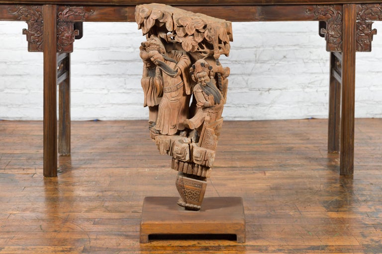 A Chinese Qing Dynasty period hand-carved wooden temple corbel from the 19th century with detailed figures and custom base. Created in China during the Qing Dynasty, this corbel comes from a temple, where it was hand-carved in wood with many