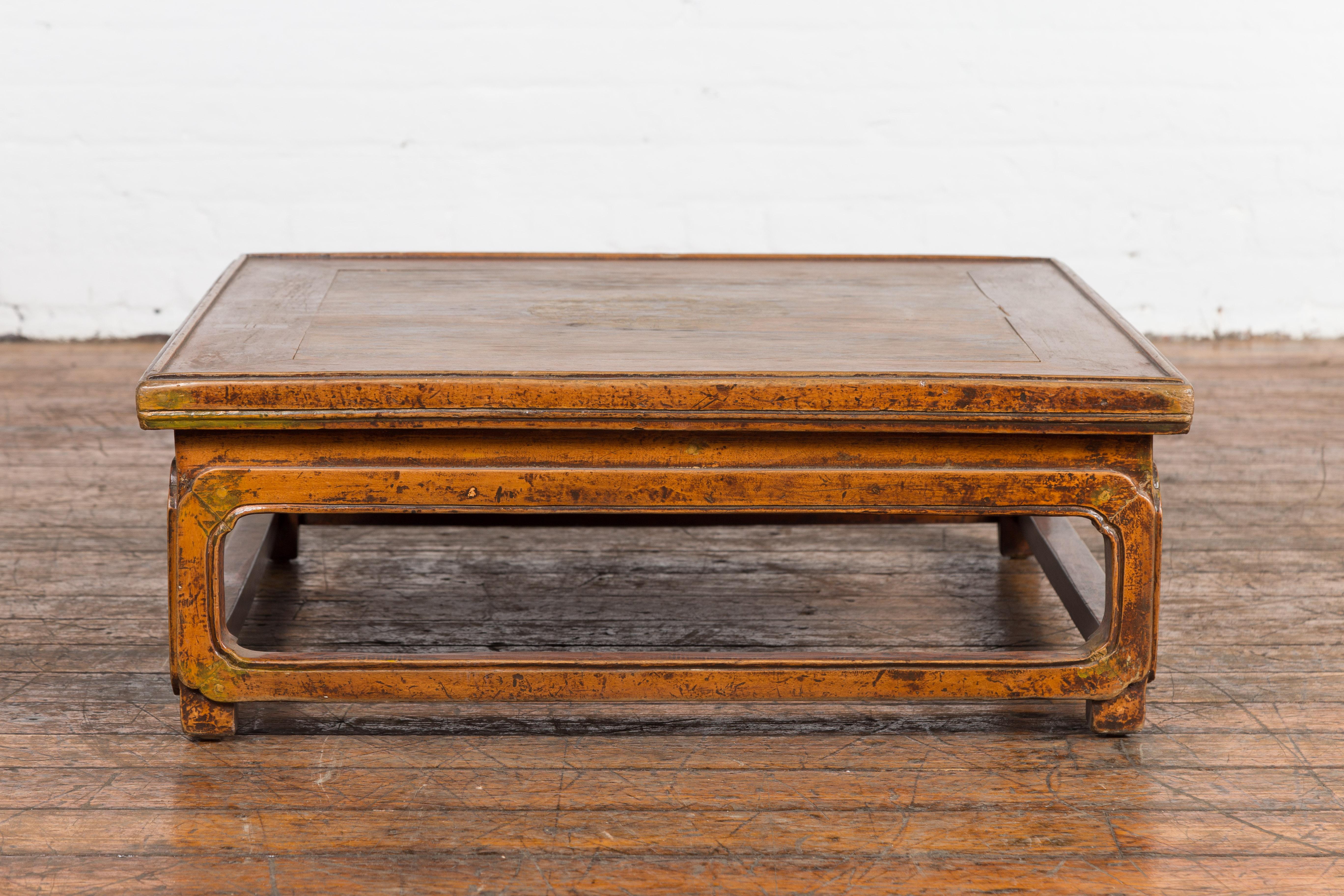 A Chinese Qing Dynasty period low Kang coffee table from the 19th century with square top and hand-painted medallion in the center. An exemplar of oriental allure and historic charm, this Chinese low Kang coffee table hails from the prestigious Qing