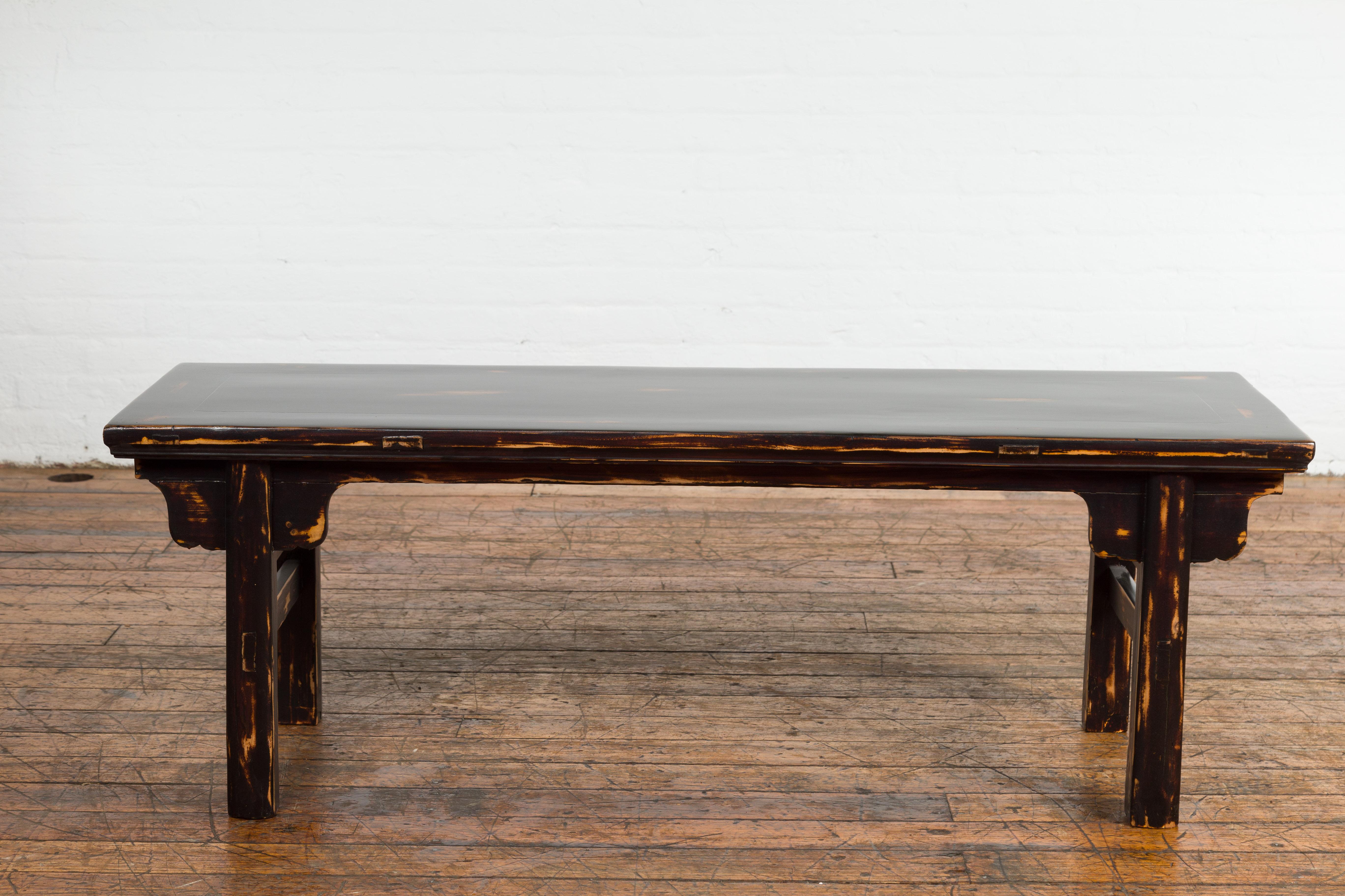 A Chinese Qing Dynasty period low table or bench from the 19th century with newly redone dark brown custom lacquer with distressing and simply carved spandrels. Immerse in the beauty of antique Chinese design with this 19th-century Qing Dynasty low