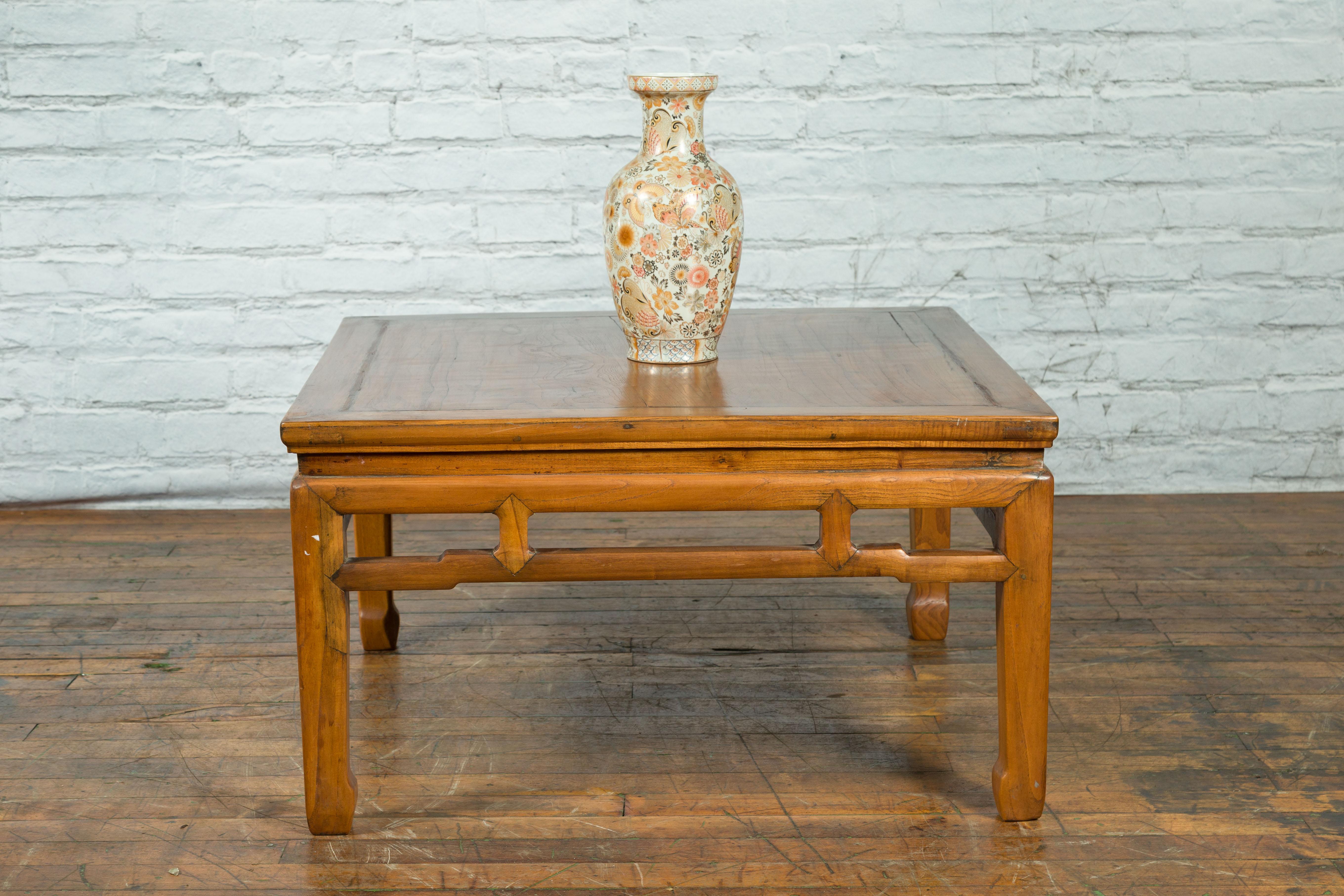 A Chinese Qing Dynasty period elm wood coffee table from the 19th century with square top, waisted apron, humpback stretcher and horse hoof legs. Created in China during the Qing Dynasty period in the 19th century, this elm wood low table which