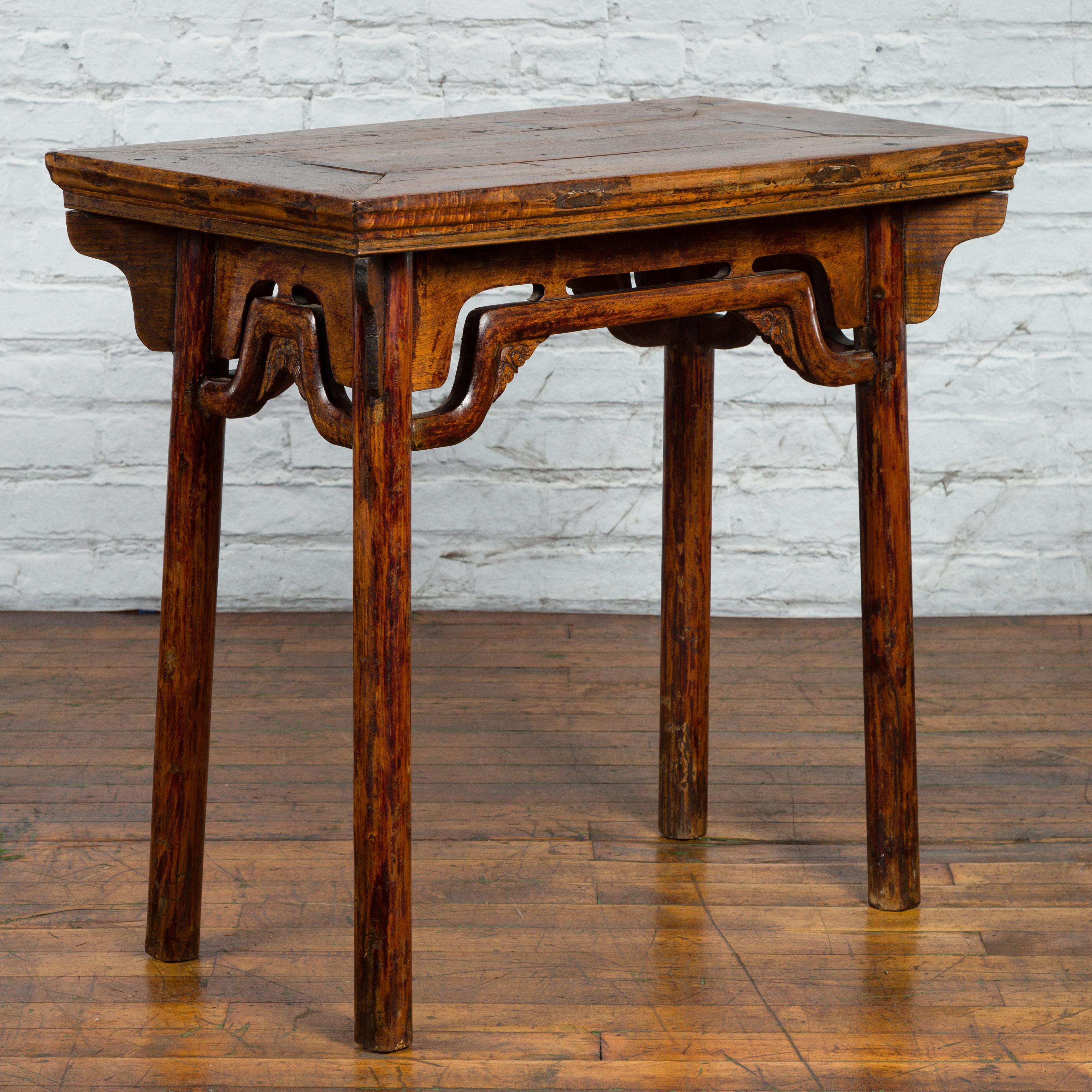 A Chinese Qing Dynasty Ming style elmwood wine table from the 19th century, with carved spandrels and humpback stretchers. Created in China during the Qing Dynasty, this elmwood wine table features a rectangular top with central board and nicely