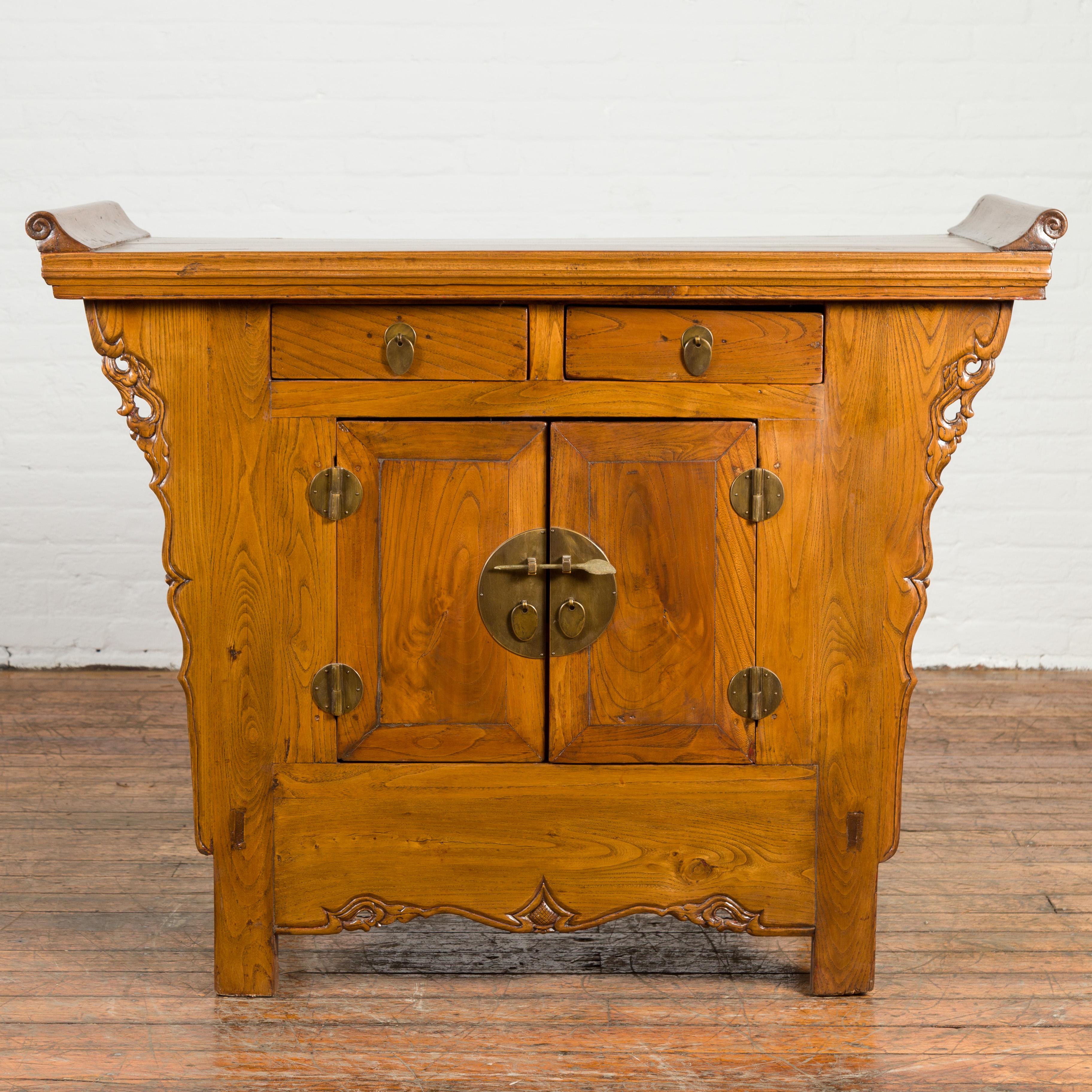 A Chinese Qing dynasty period altar cabinet from the 19th century, with natural finish, everted flanges, two drawers over double doors and carved sides. Created in China during the 19th century, this Chinese altar cabinet features a rectangular top