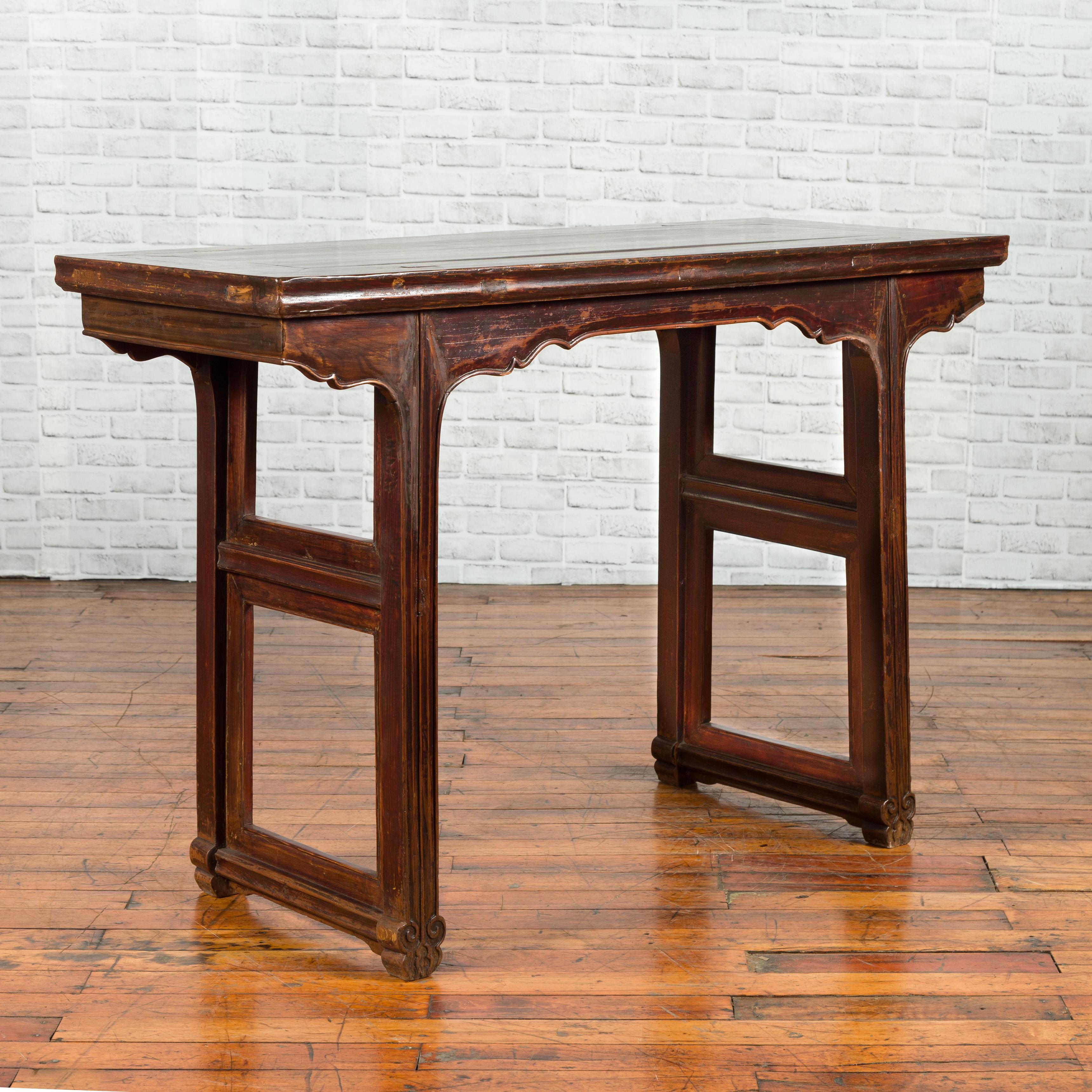 A Chinese Qing Dynasty period altar console table from the 19th century, with carved apron and dark patina. Created in China during the Qing Dynasty, this console table features a rectangular top with central board, sitting above a carved apron with