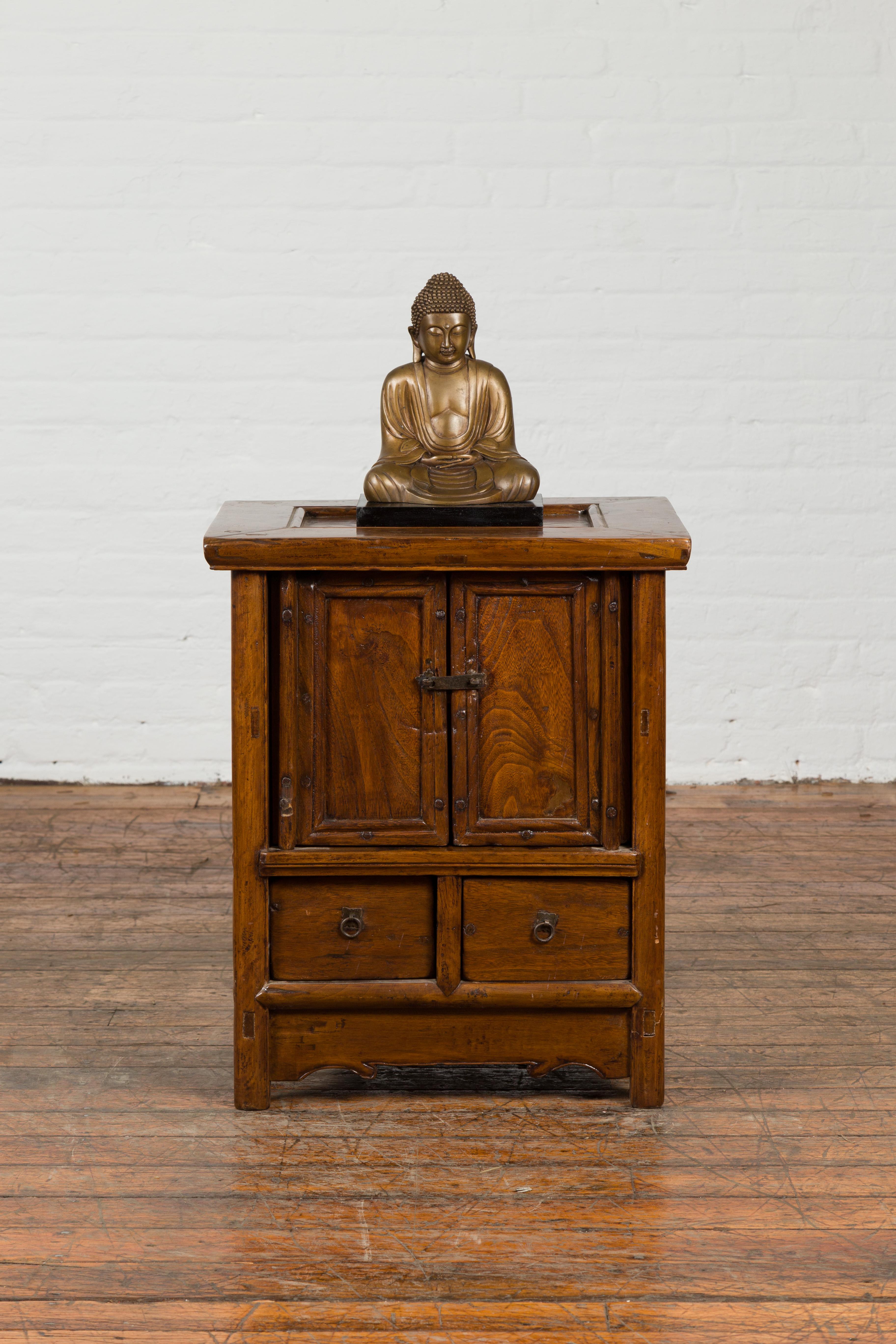 A Chinese Qing dynasty period small bedside cabinet from the 19th century, with doors and drawers. Created in China during the Qing dynasty period, this bedside cabinet features a rectangular top with inset panel, overhanging two petite doors