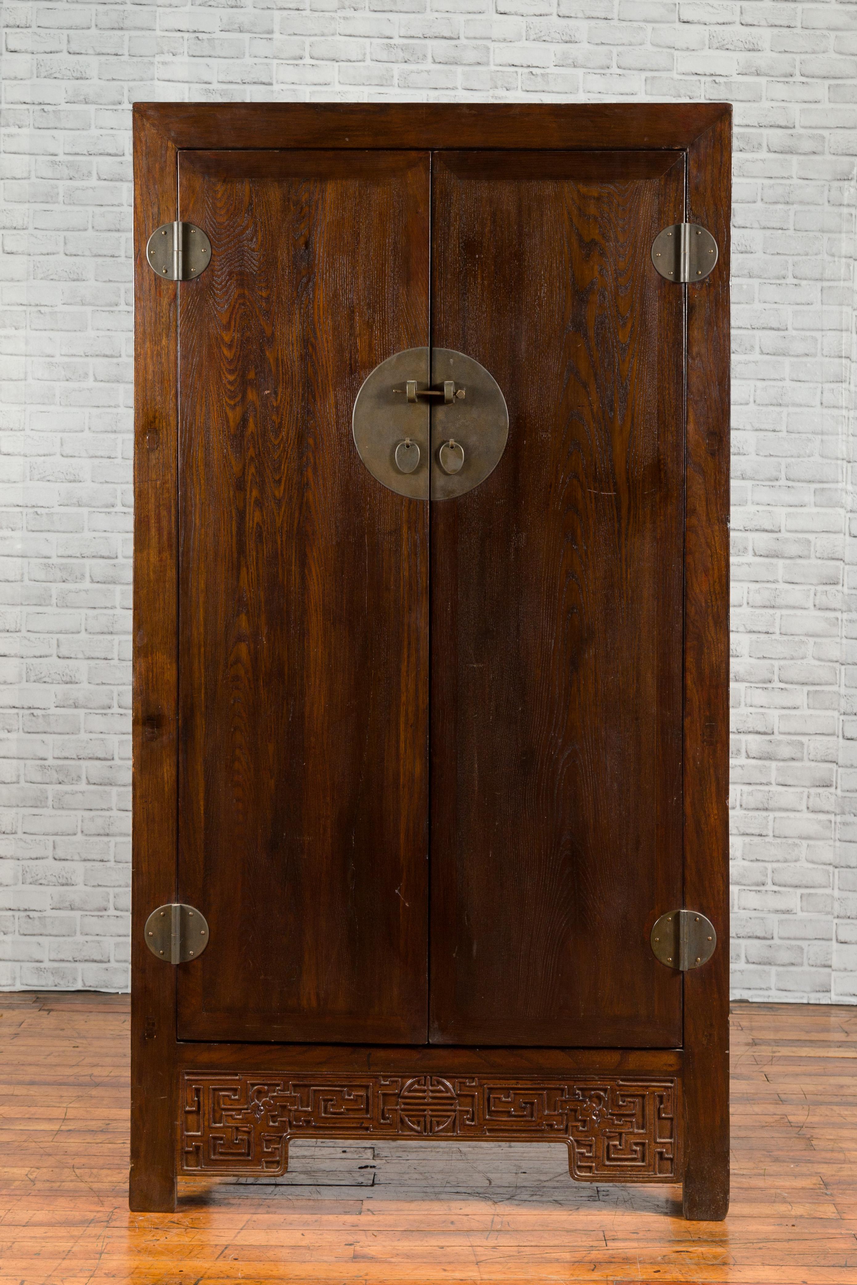 A Chinese Qing Dynasty period large cabinet from the 19th century, with carved apron and hidden drawers. Created in China during the Qing Dynasty period, this large brown cabinet features a linear silhouette perfectly complimented by the dark brown