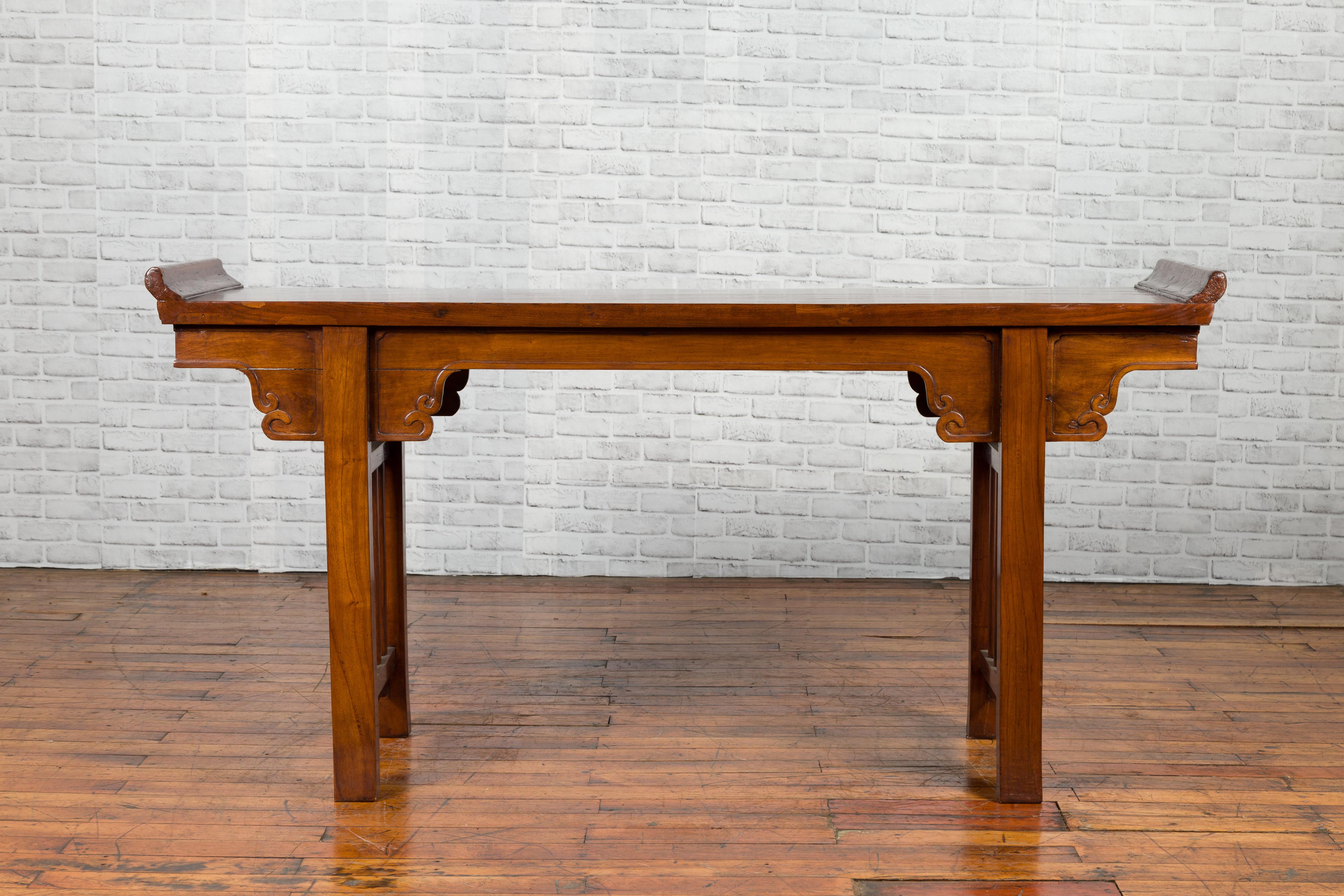 A Chinese Qing Dynasty period elmwood altar console table from the 19th century, with carved spandrels and everted flanges. Created in China during the 19th century, this console table features a single plank rectangular top flanked with everted