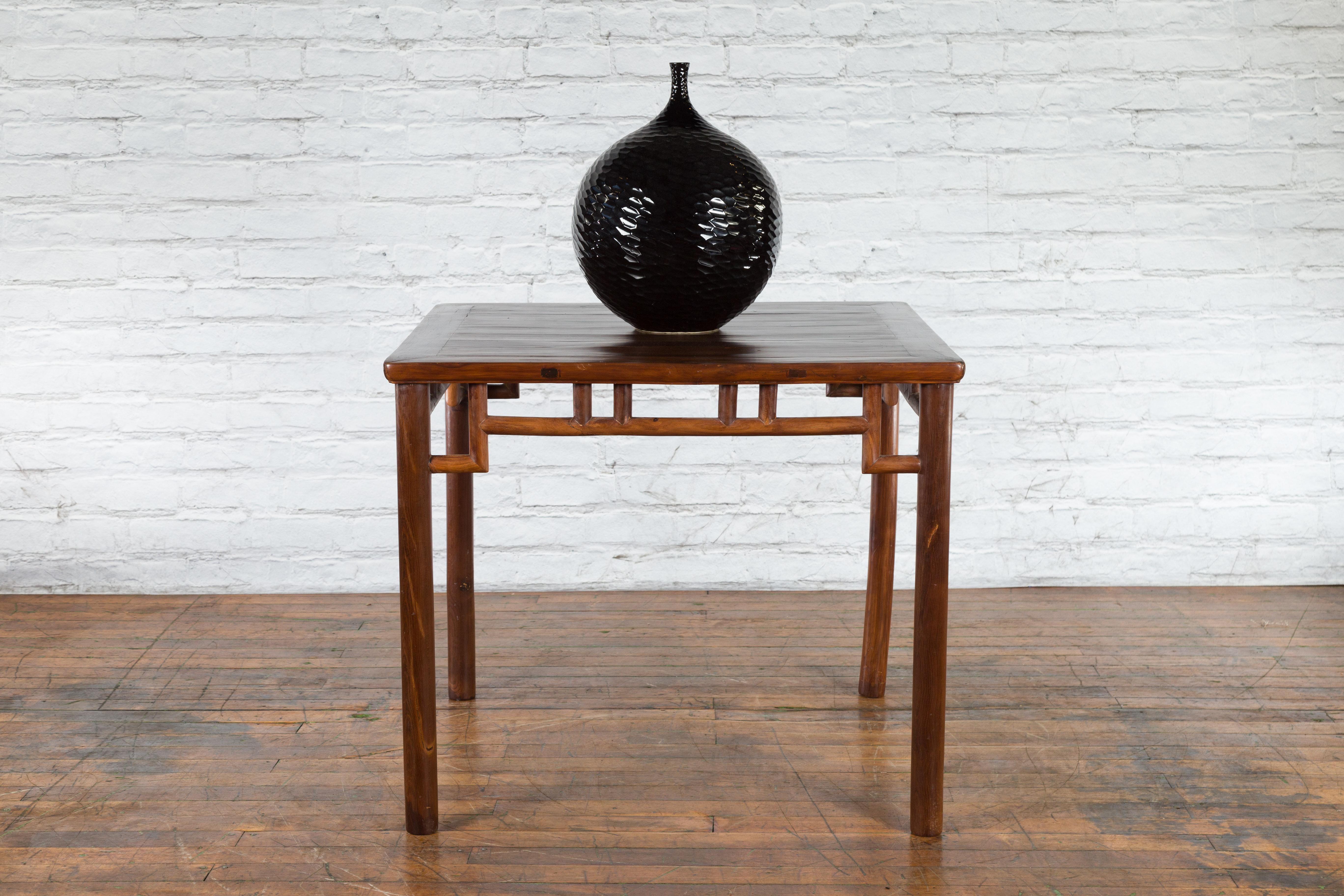 A Chinese Qing Dynasty period game table from the 19th century with humpback stretchers and pillar strut motifs. Created in China during the Qing Dynasty in the 19th century, this game table features a square planked top sitting above an openwork