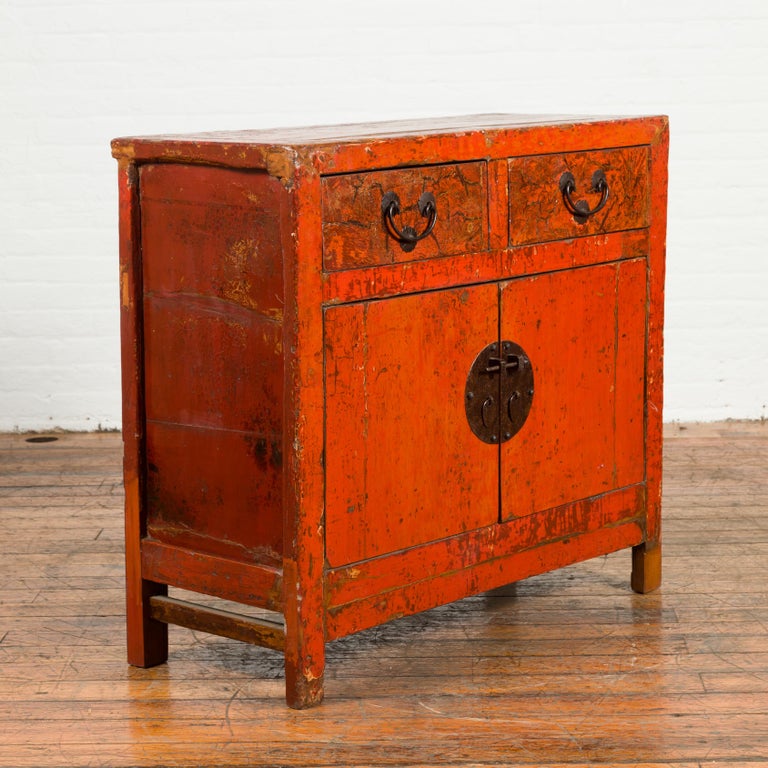 A Chinese Qing dynasty red lacquer small cabinet from the 19th century, with two drawers and two doors. Created in China during the Qing dynasty period, this red lacquered cabinet features two drawers with distressed finish, sitting above a pair of