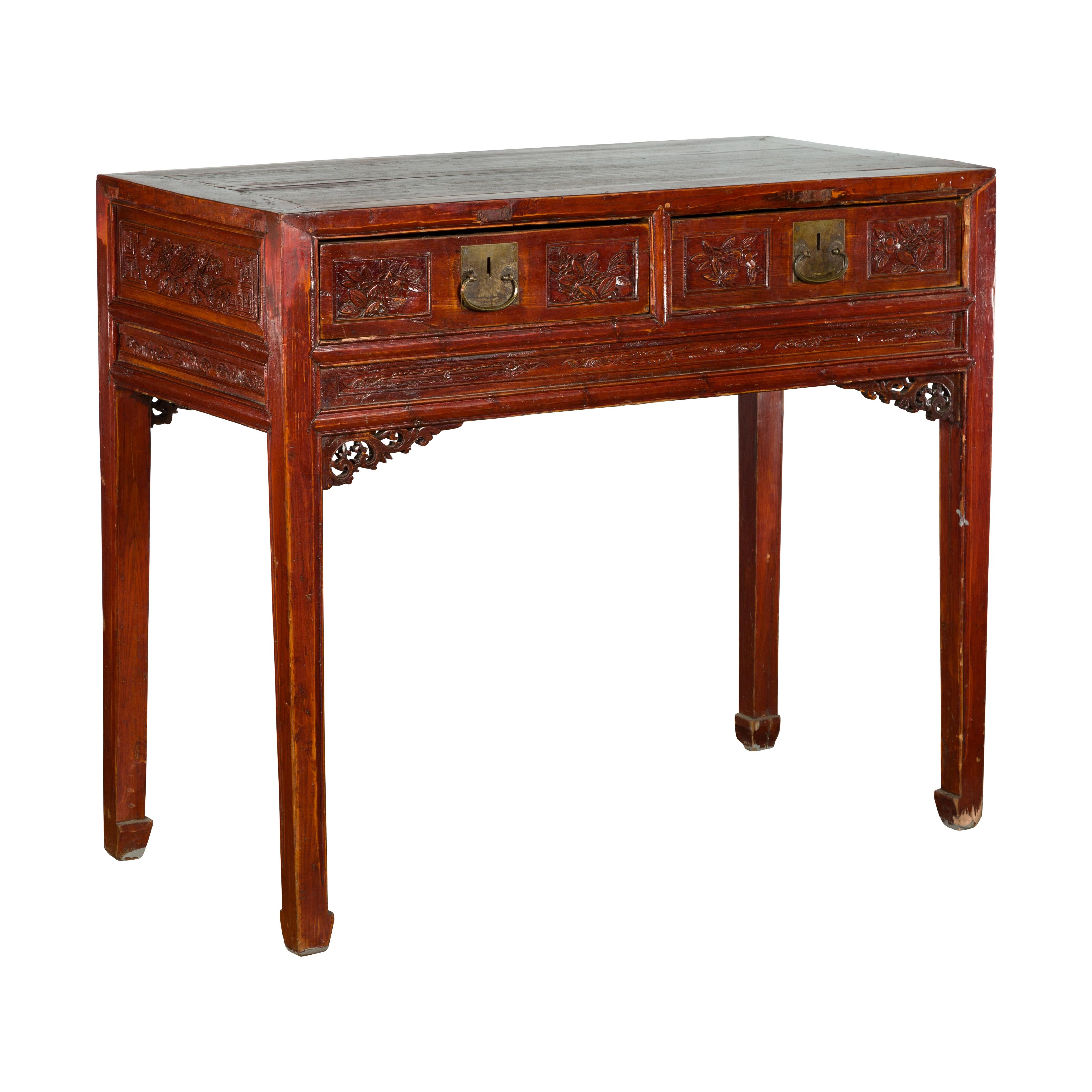 An antique Chinese Qing Dynasty period two-drawer console table from the 19th century, with carved spandrels and floral motifs. Created in China during the Qing Dynasty period, this reddish brown lacquered table features a rectangular planked top