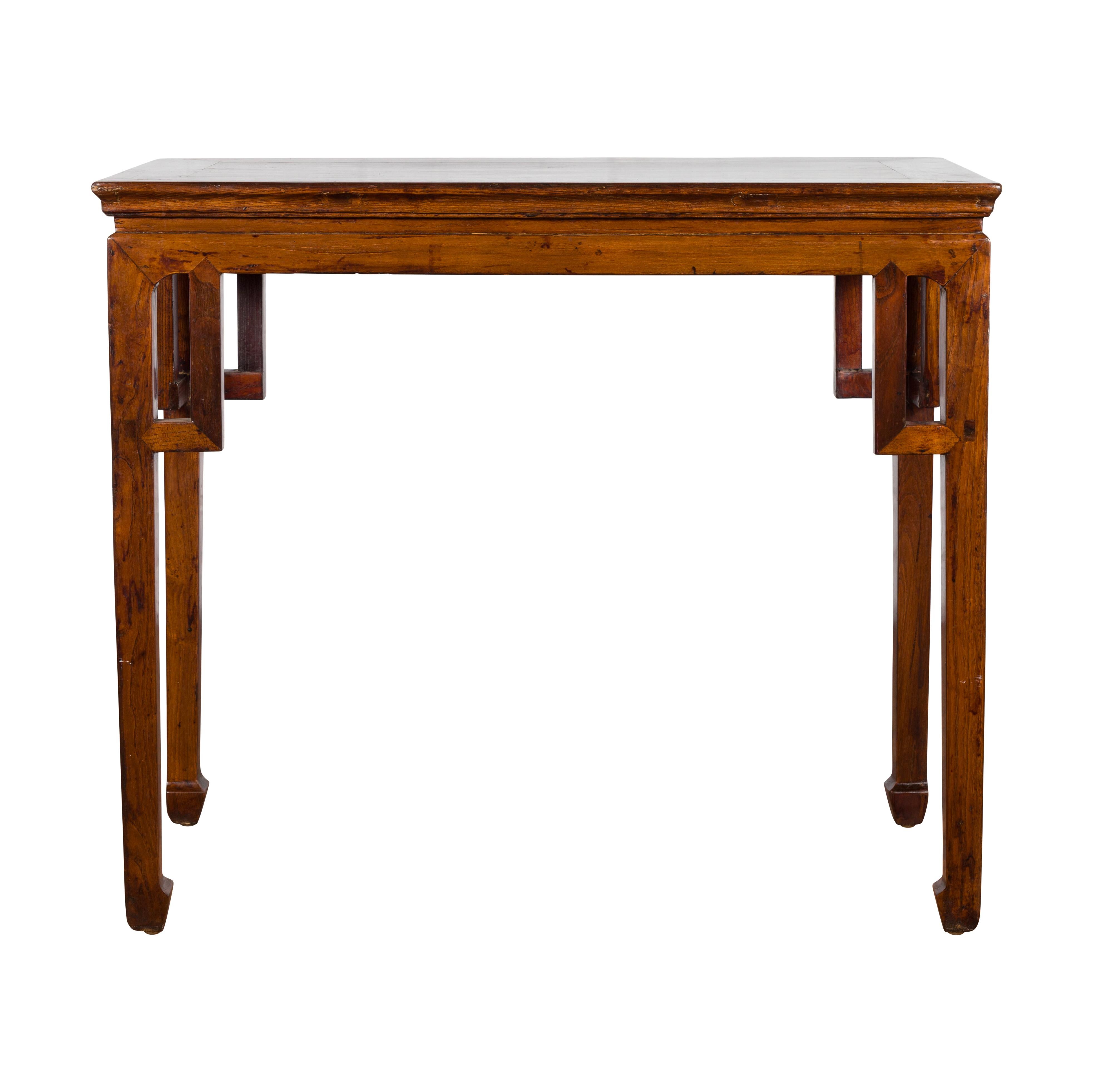 A Chinese Qing Dynasty period wooden wine table from the 19th century, with linear spandrels and horse hoof feet. Created in China during the Qing Dynasty, this wine table features a rectangular waisted top sitting above four straight legs connected