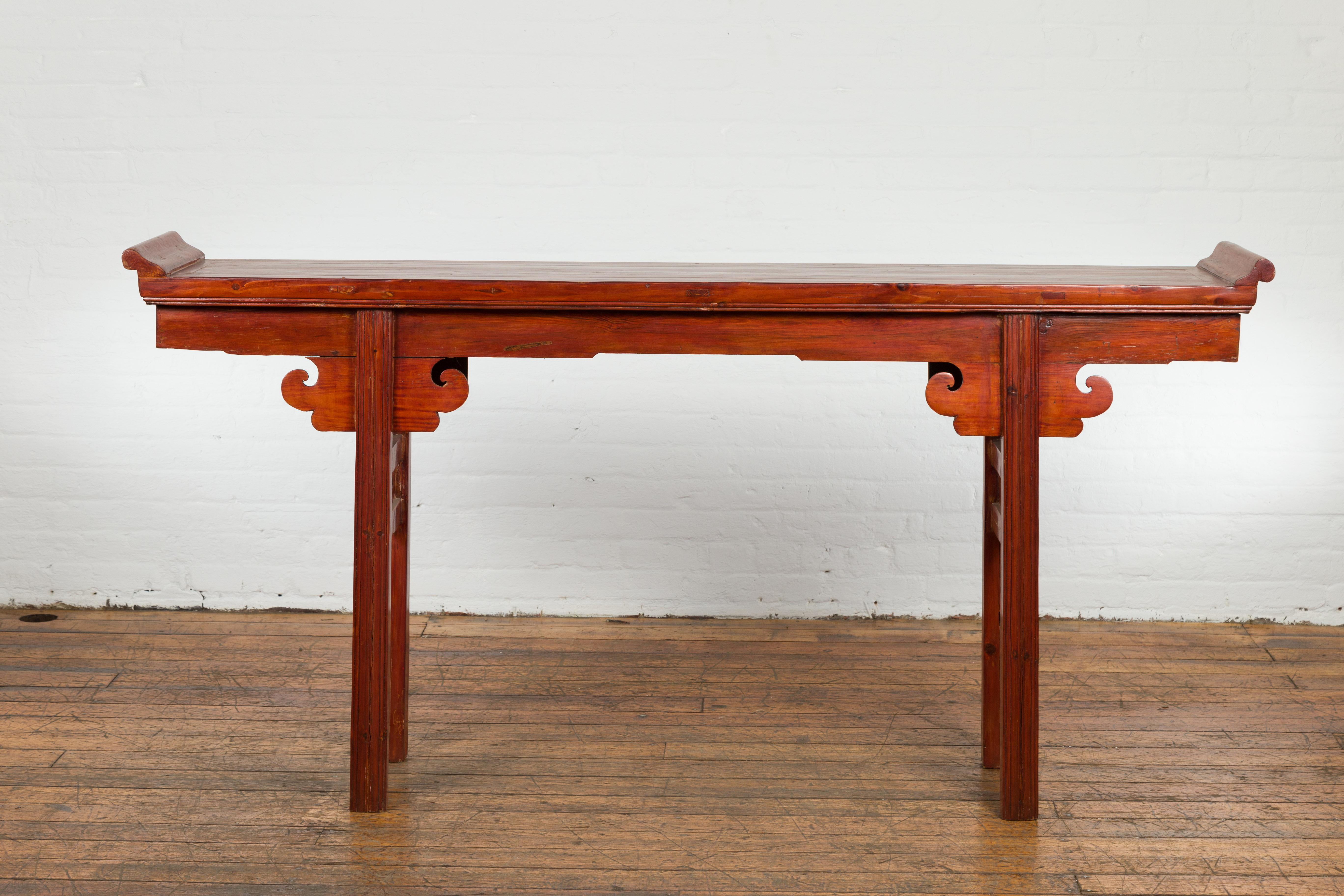A Chinese Qing Dynasty period altar console table from the 19th century, with everted flanges, carved cloud motifs and orange, red and brown lacquer. Created in China during the Qing Dynasty period in the 19th century, this altar table attracts our