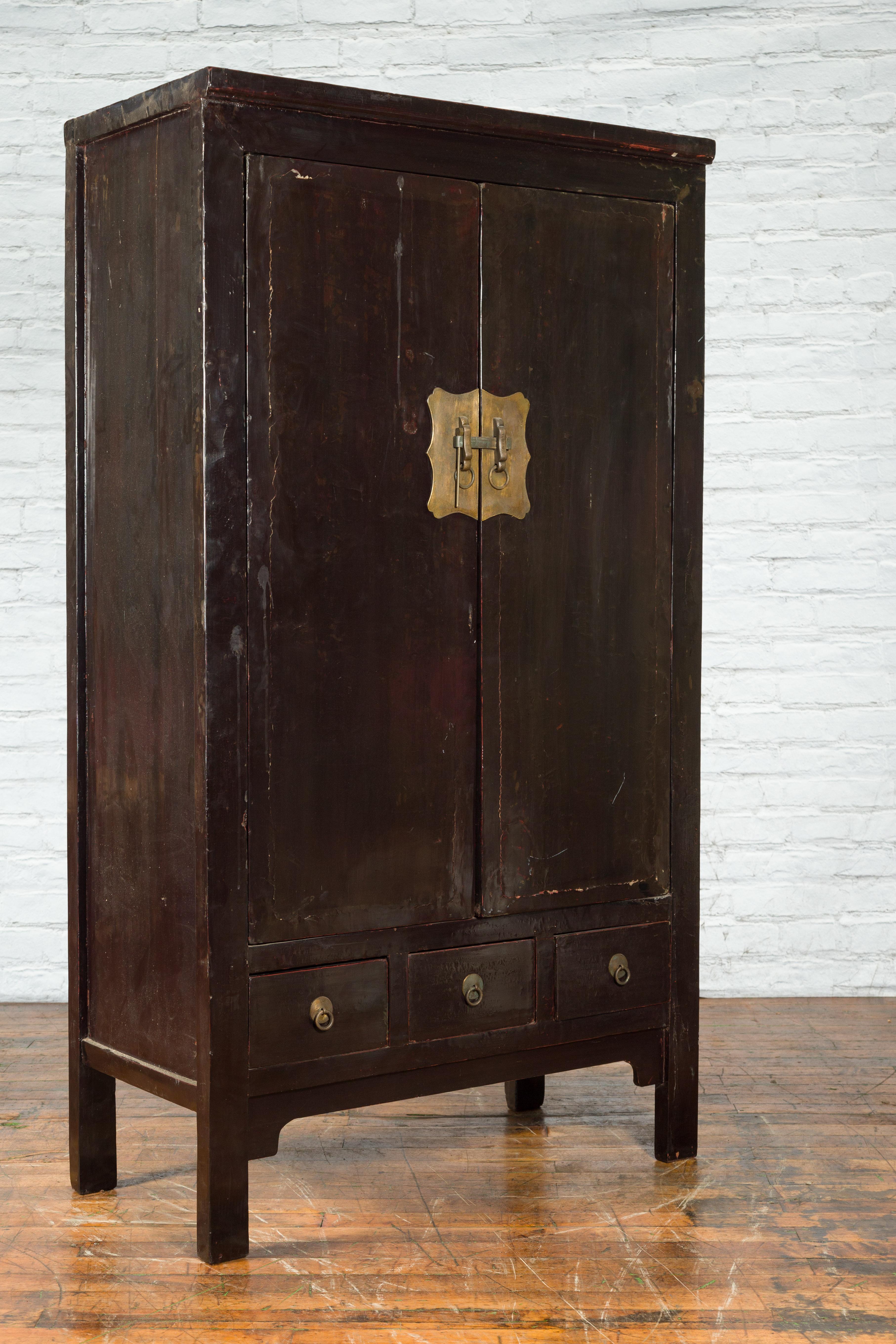 A Chinese Qing Dynasty period wardrobe from the early 19th century with dark brown lacquer, brass hardware, doors, drawers and shelves. Created in China during the Qing Dynasty period in the early years of the 19th century, this wooden wardrobe