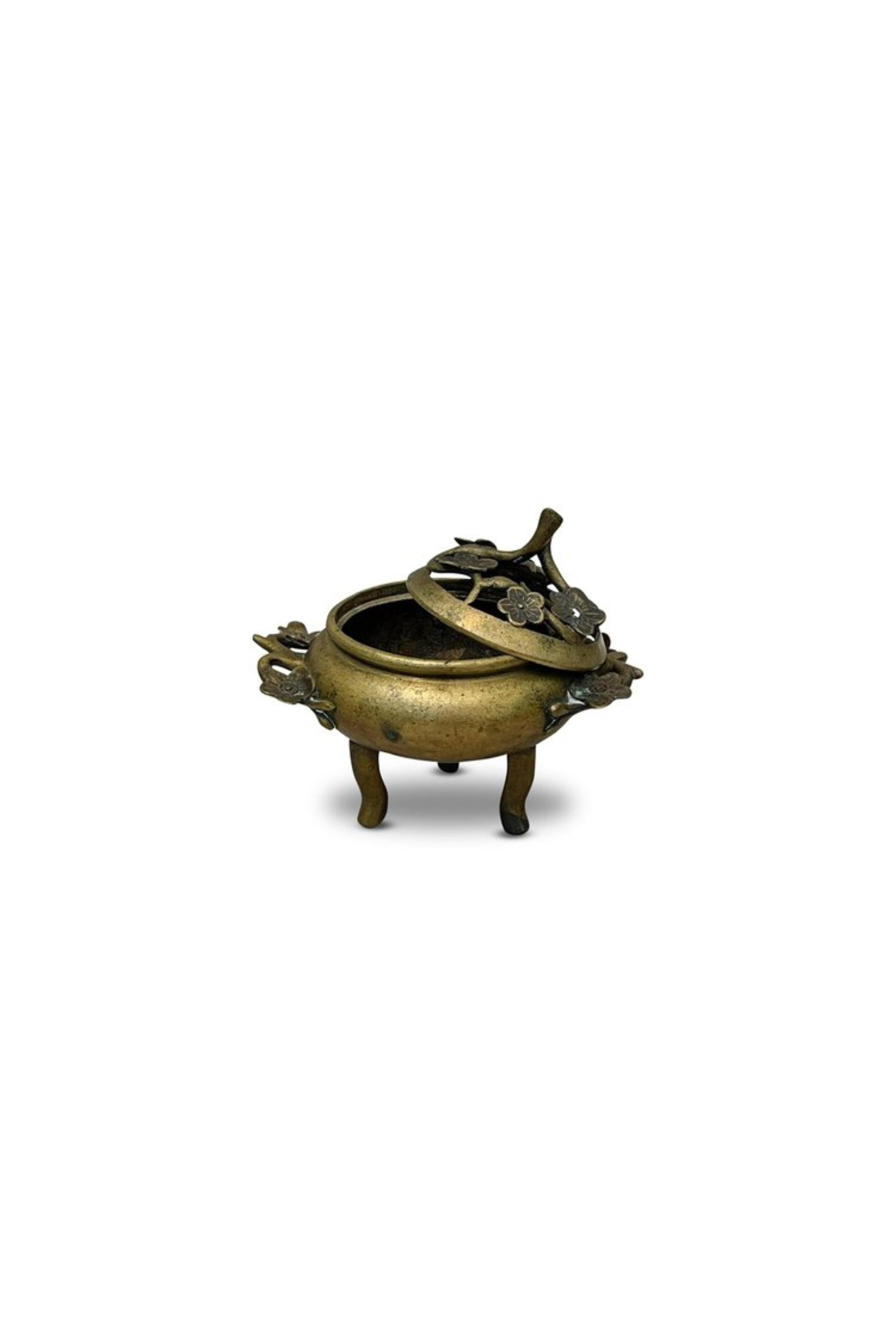 This tripod censer is an exquisite piece from the Qing Dynasty, showcasing a delicate cherry blossoms design. The censer features intricate gilt bronze craftsmanship, highlighting the elegant floral motifs that adorn its surface. Supported by three