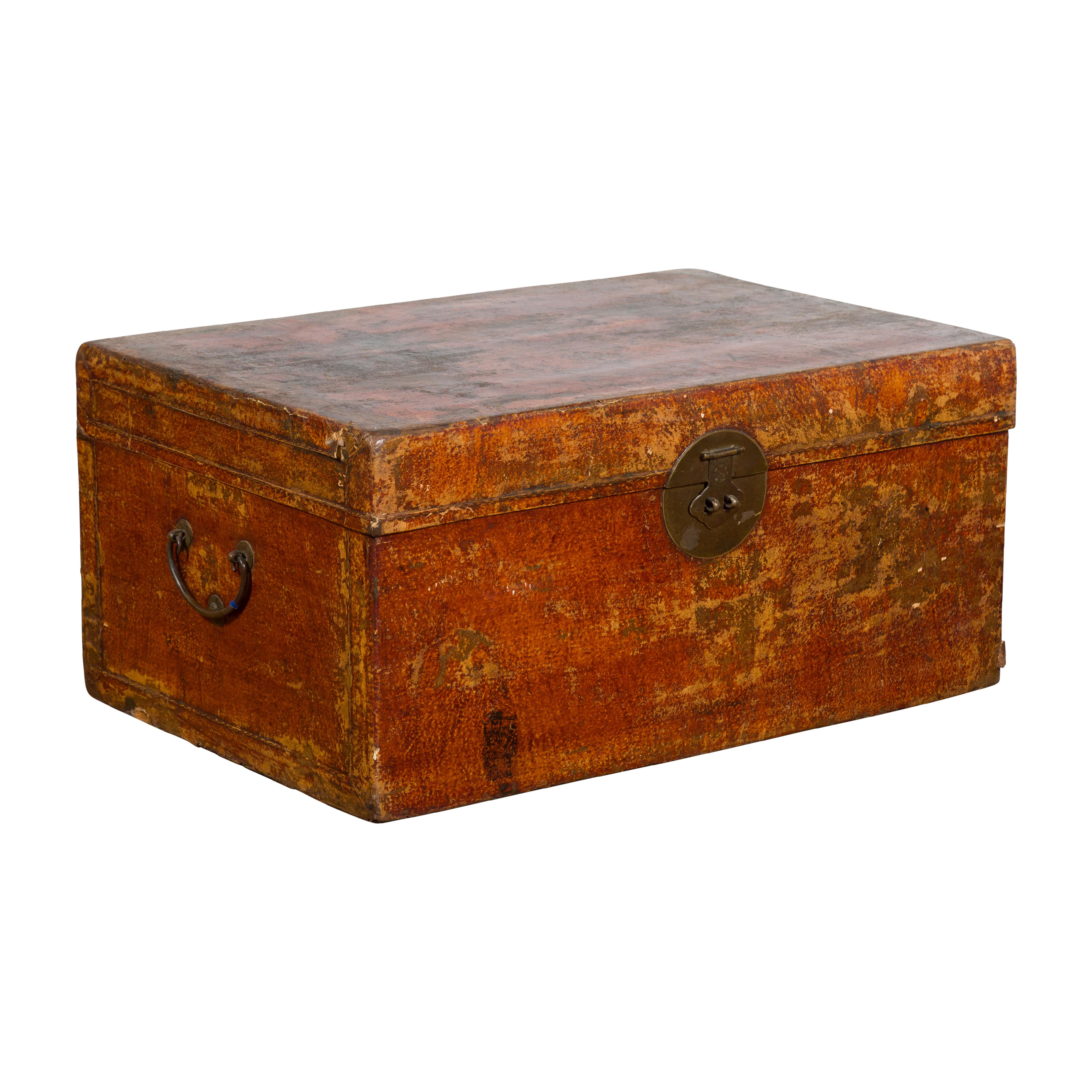 A Chinese antique Qing Dynasty period storage trunk from the 19th century made of red lacquered leather with distressed patina, Ming style brass hardware and lateral C-scroll handles. Created in China during the Qing Dynasty period in the 19th