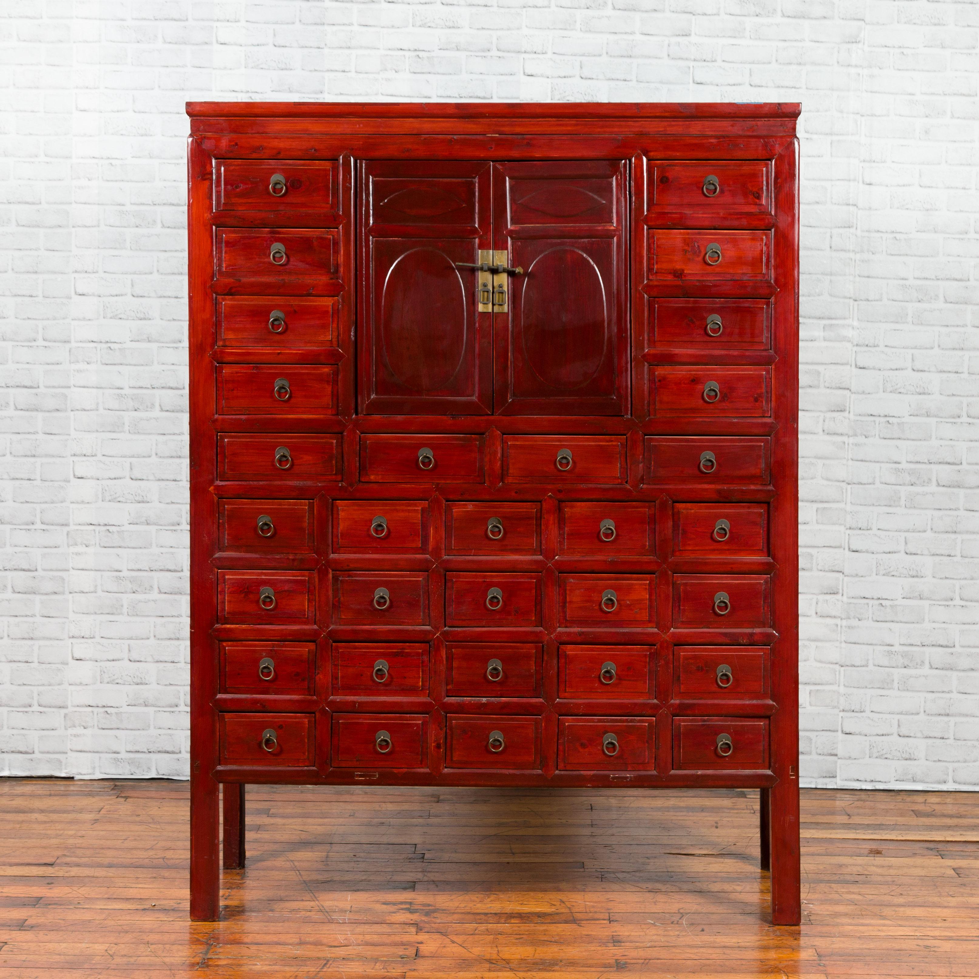 A Chinese red lacquered apothecary-inspired cabinet from the early 20th century, with 32 drawers and petite double doors. Created in China during the second quarter of the 20th century, this cabinet captures our attention with its red lacquered