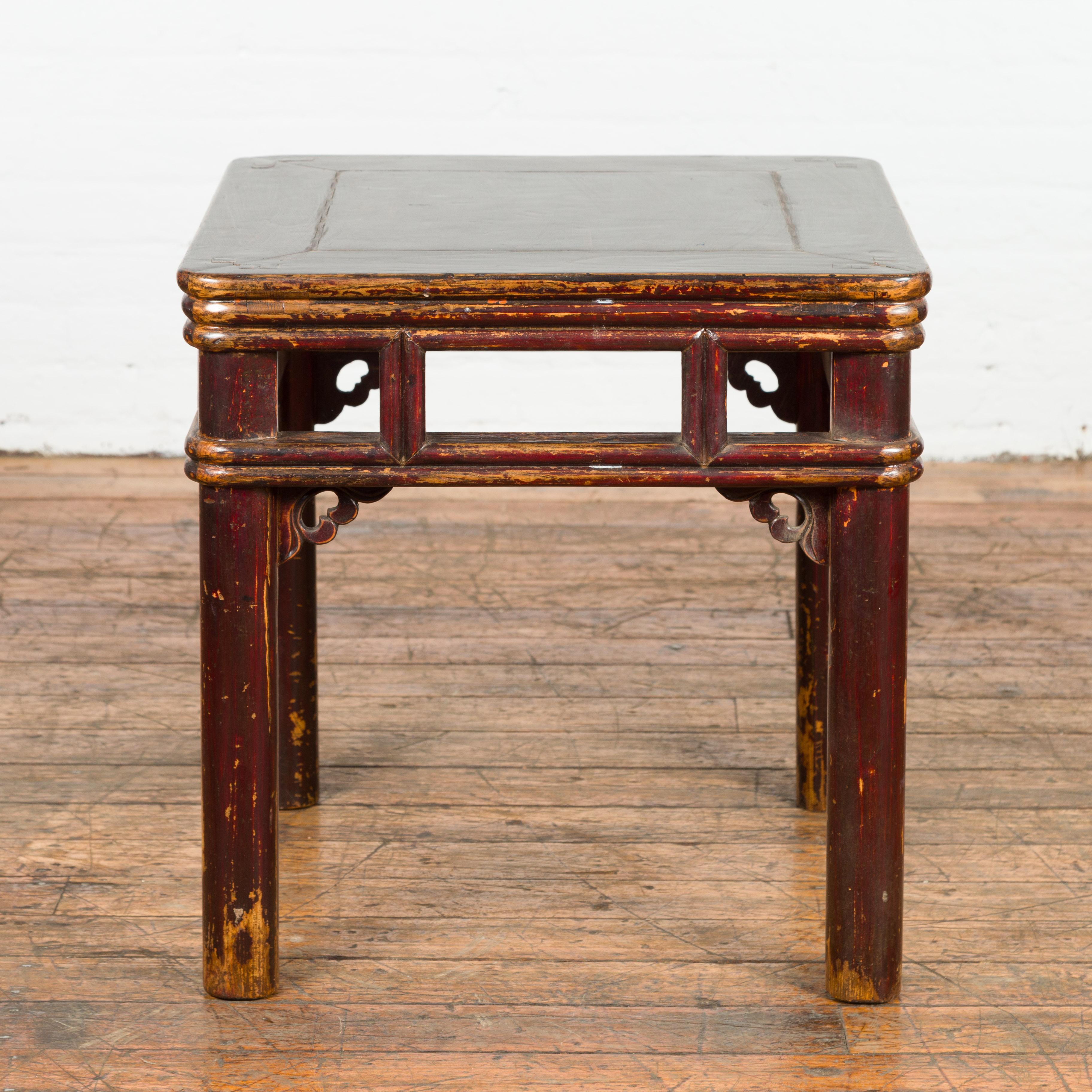 A Chinese Qing Dynasty period elm wood stool or side table from the 19th century, with open apron, carved spandrels, pillar strut motifs and distressed patina. Discover the allure of historical craftsmanship with this Qing Dynasty period Chinese elm
