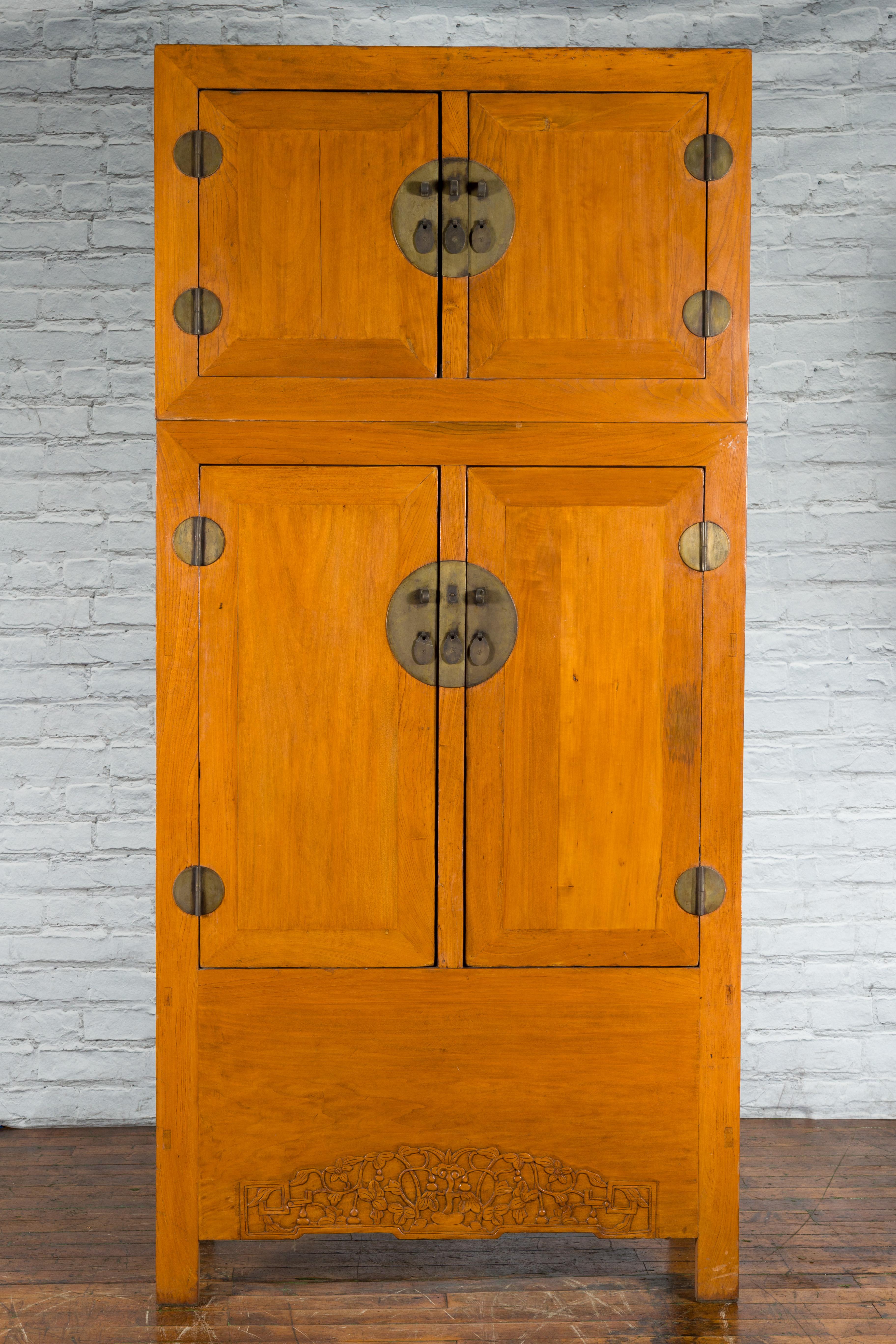 A Chinese Qing Dynasty period wooden compound cabinet from the 19th century, with four doors, foliage-carved apron and brass medallion hardware. Created in China during the Qing Dynasty period in the 19th century, this large compound wardrobe