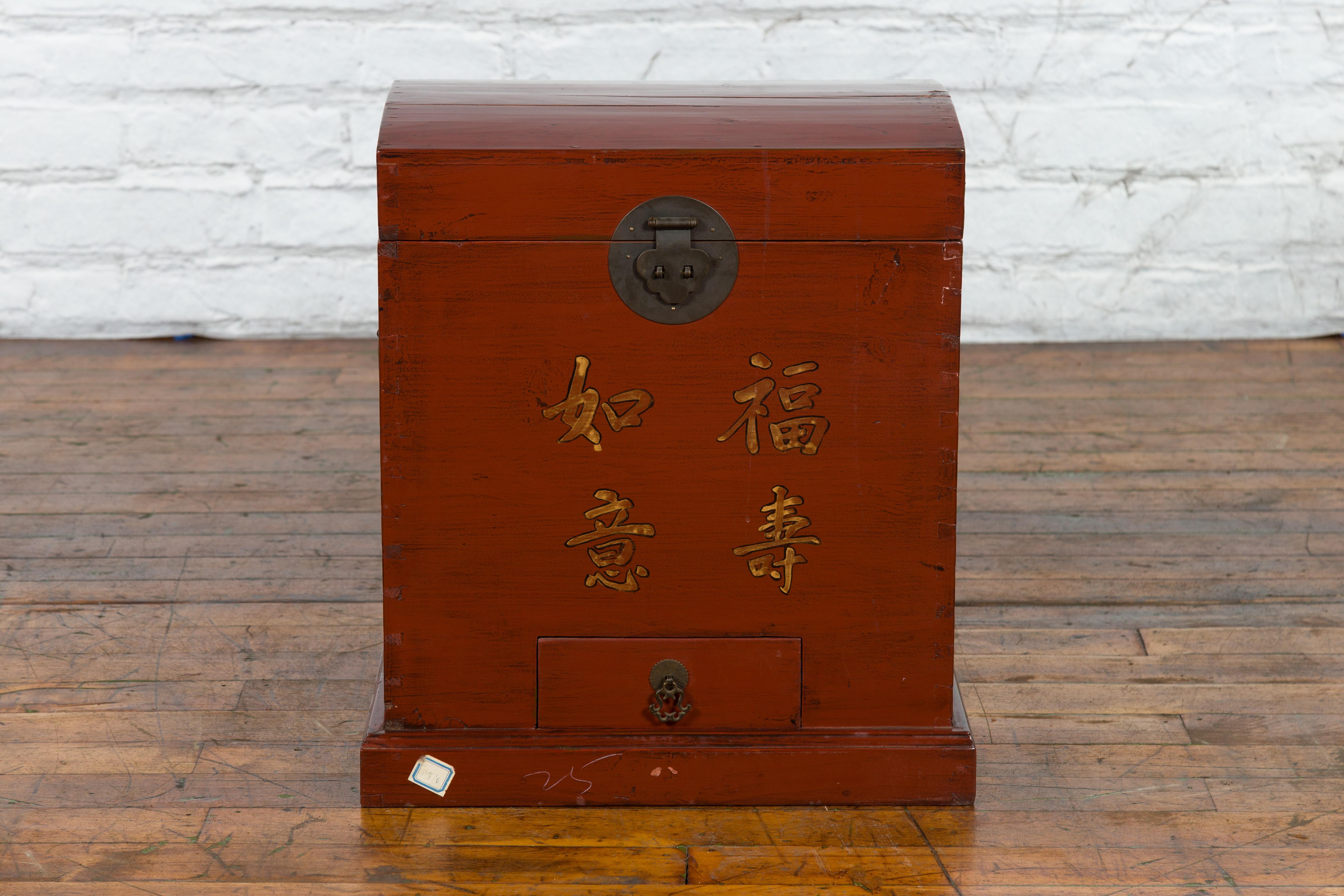 An antique Chinese Qing Dynasty period red lacquer treasure chest from the 19th century with gilded calligraphy, low drawer and brass hardware. Created in China during the Qing Dynasty period in the 19th century, this treasure chest showcases a red
