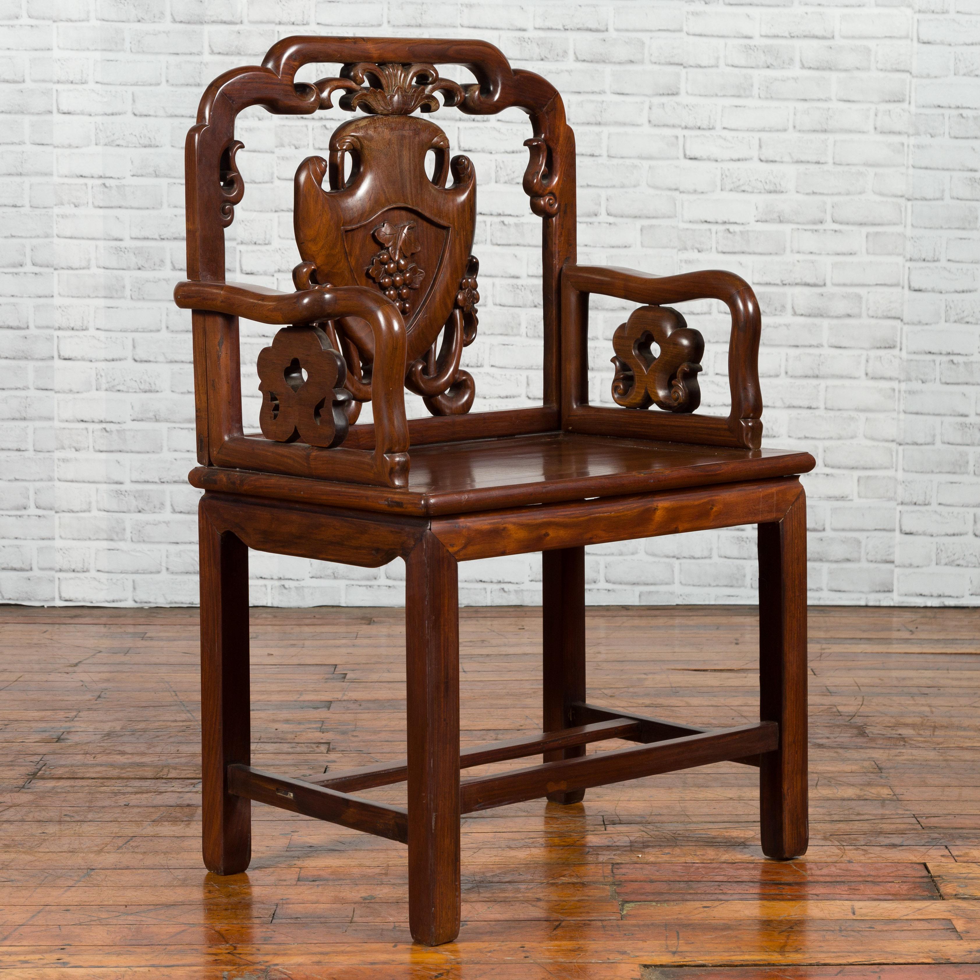 A Chinese Qing Dynasty period rosewood armchair from the 19th century, with hand carved splat and arm supports. Created in China during the 19th century, this rosewood chair attracts our attention with its stunning back, adorned with grapes carved