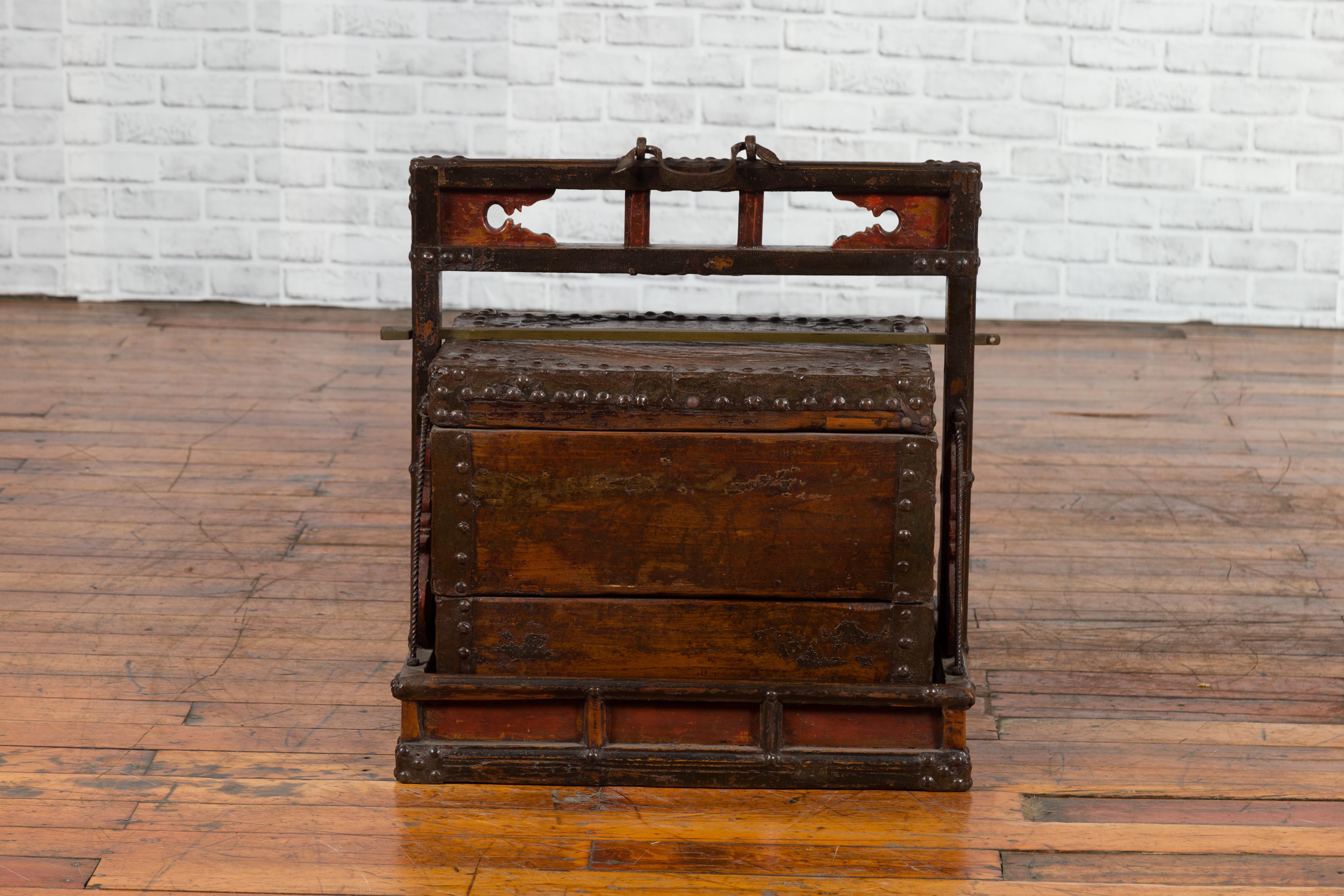 A Chinese Qing dynasty period wooden tiered wedding box from the 19th century, with carved sides, handle and nailheads. Created in China during the 19th century, this wedding box features a linear silhouette, accented with metal braces and