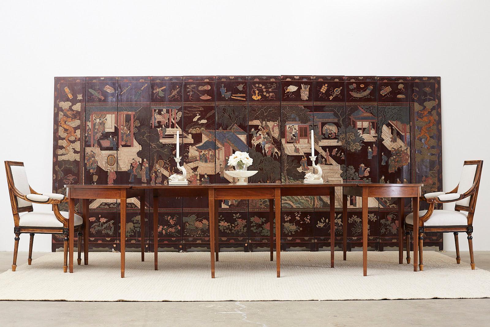 Captivating Chinese late 19th century Qing dynasty twelve-panel lacquered Coromandel screen. Intricately carved courtyard scene amid pagodas and trees. Bordered with floral and foliate carvings on bottom with scholars objects on the top. Each