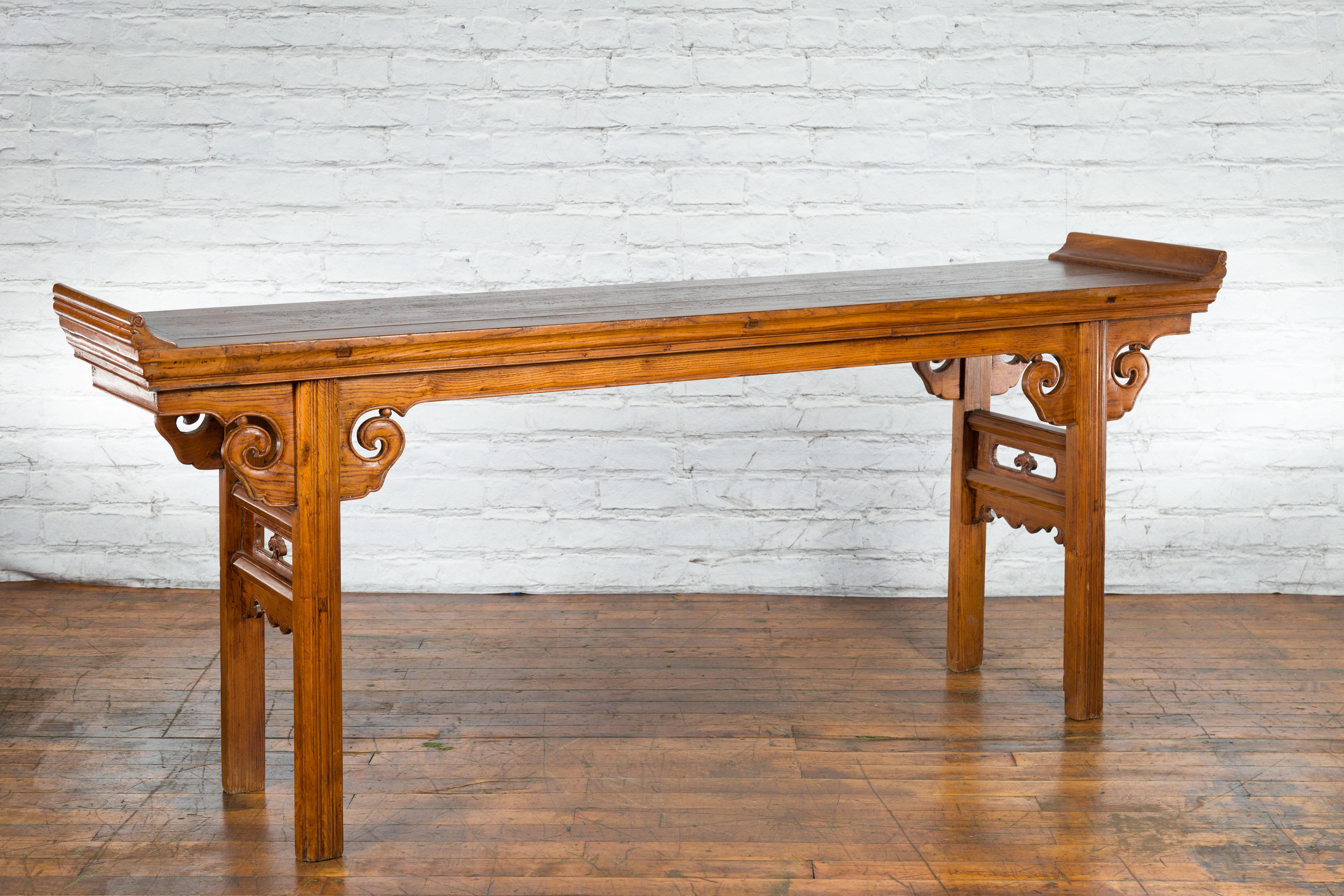 A Chinese Qing Dynasty period wooden altar console table from the 19th century with everted flanges, scrolling spandrels and carved side panels. Created in China during the 19th century, this altar table attracts our attention with its brown patina