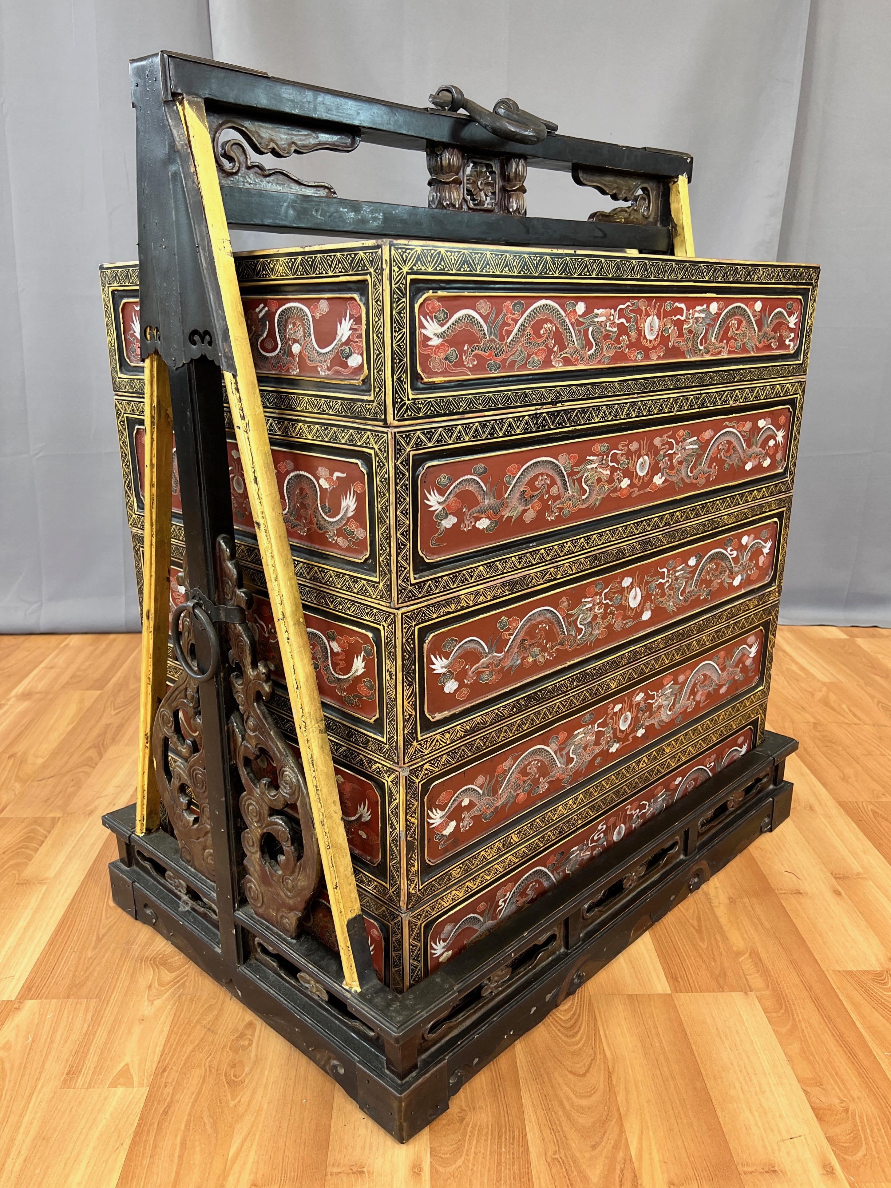 A large and impressive early 20th century Chinese Qing dynasty era hand-decorated lacquered and giltwood five-tier wedding dowry travel cabinet with carved wood and cast iron elements.

Comprised of five removable lacquered boxes with oxblood