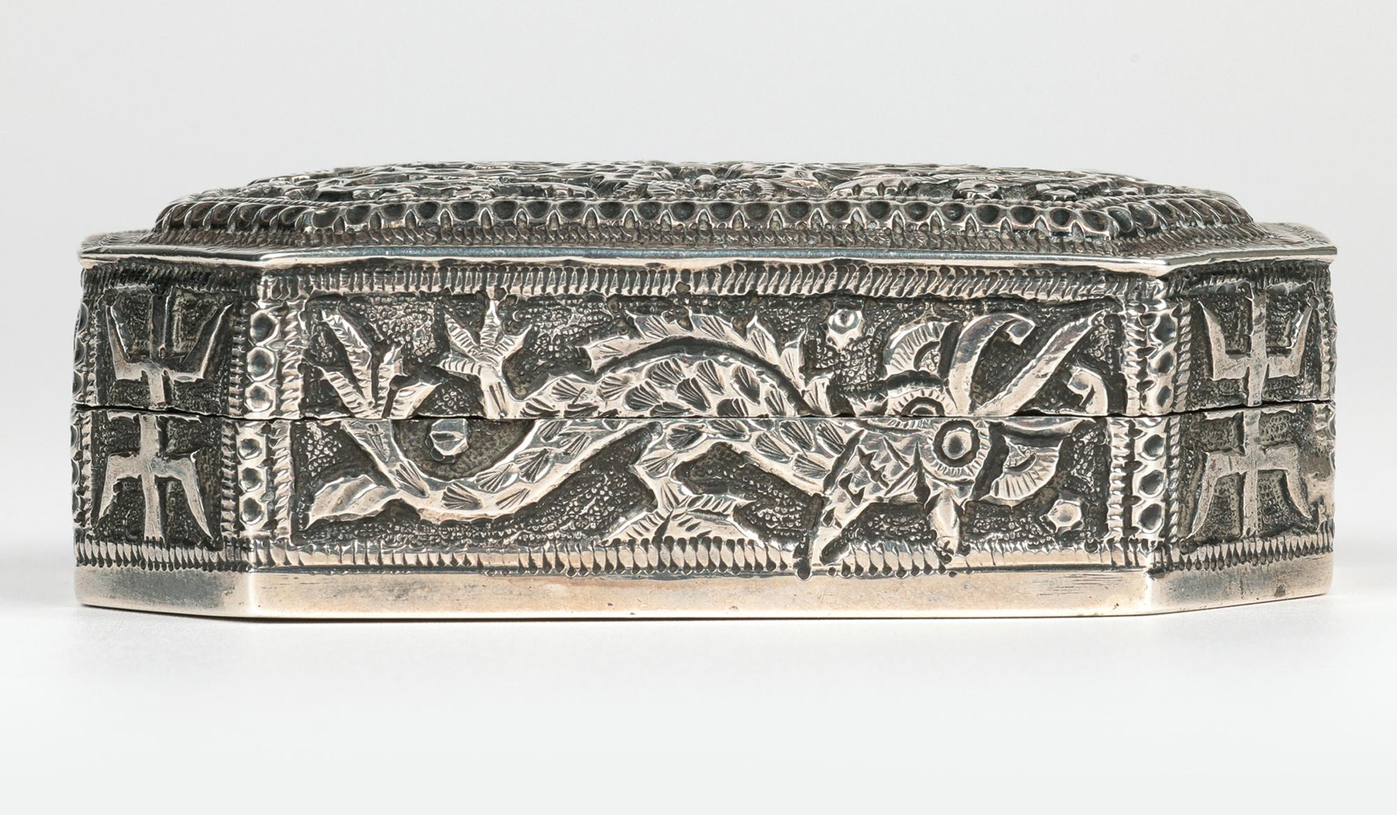 Excepcional caja antigua china qing de plata con criaturas estilizadas y símbolos chinos que data de finales del siglo XIX. La caja, de forma rectangular y muy elaborada, tiene las esquinas en ángulo con un panel en relieve en la tapa. La portada