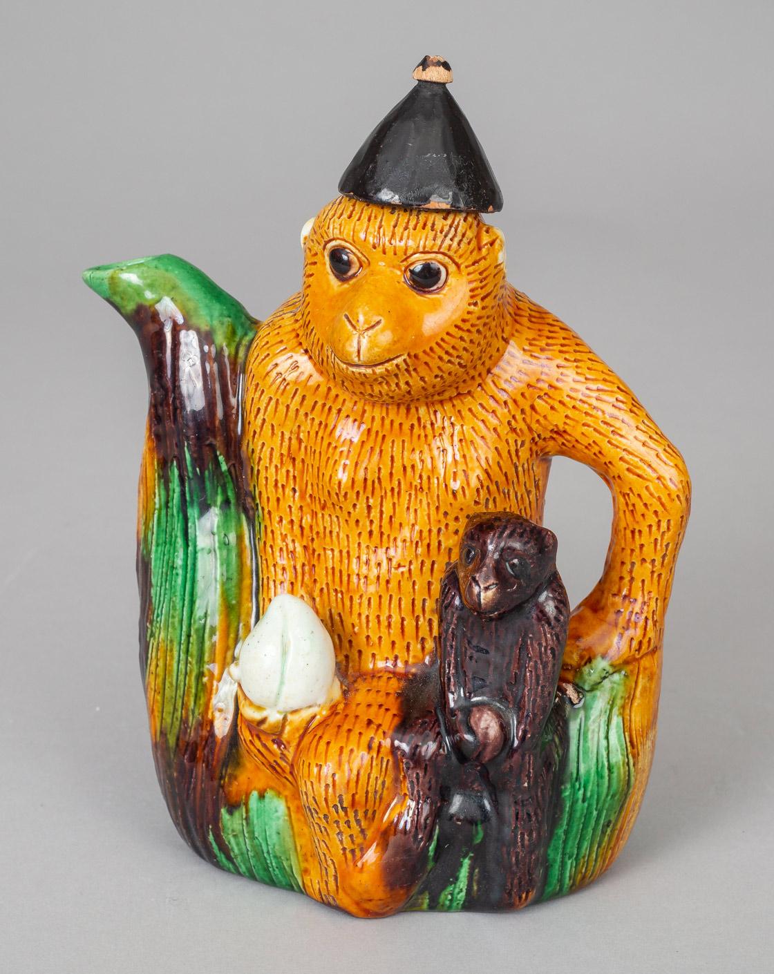 Chinese Qing dynasty Guangxu period porcelain tea pot in the form of a monkey holding a peach with a young monkey sitting on its lap also holding a peach, decorated in sancai colors of yellow, green and brown. The arm forms the handle and the