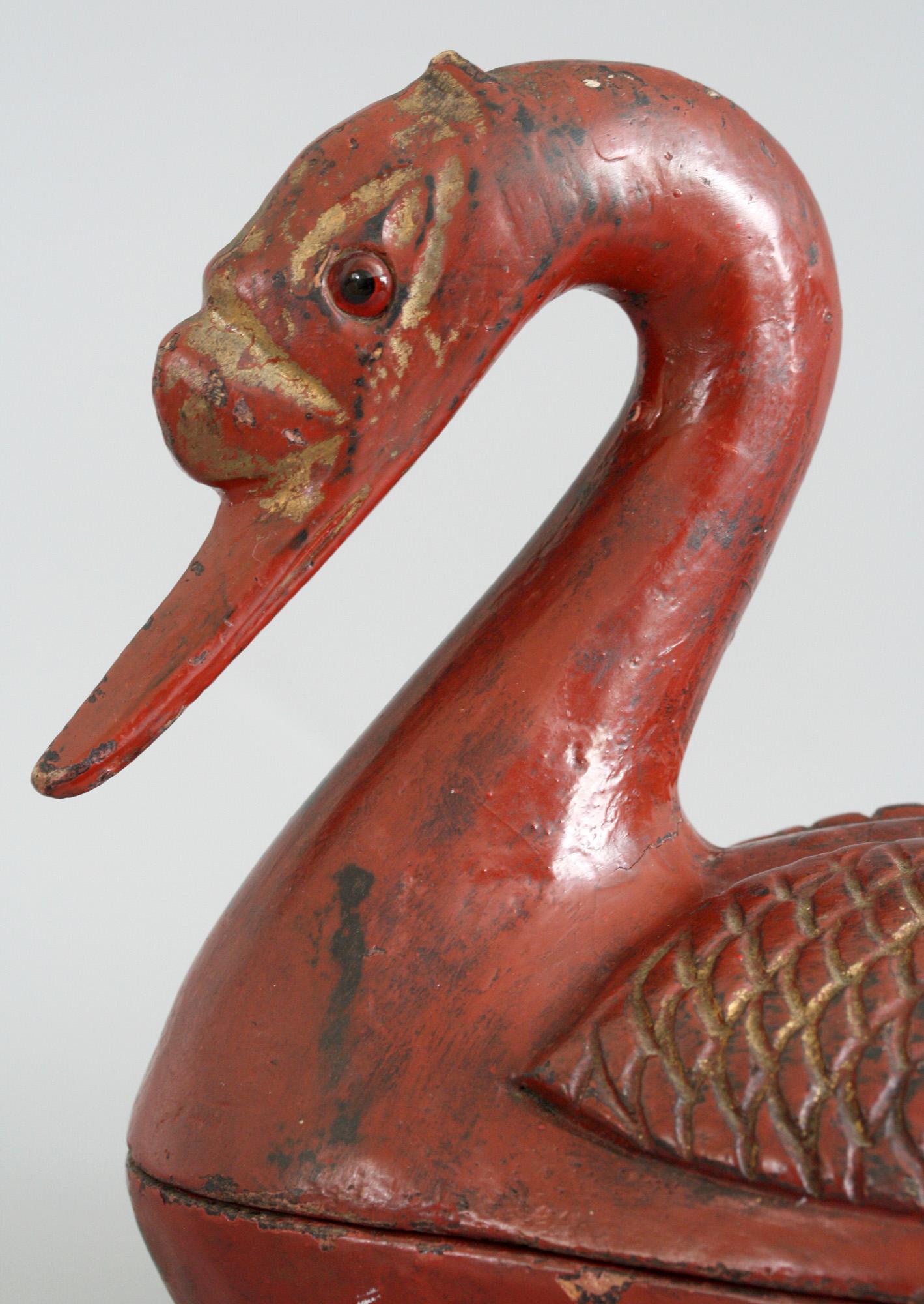 An unusual antique Chinese Qing red lacquered wooden lidded box modeled as a duck dating from the later 19th century. The duck is modeled seated with its legs resting beneath its body which forms the box. The cover is formed of the duck’s upper body