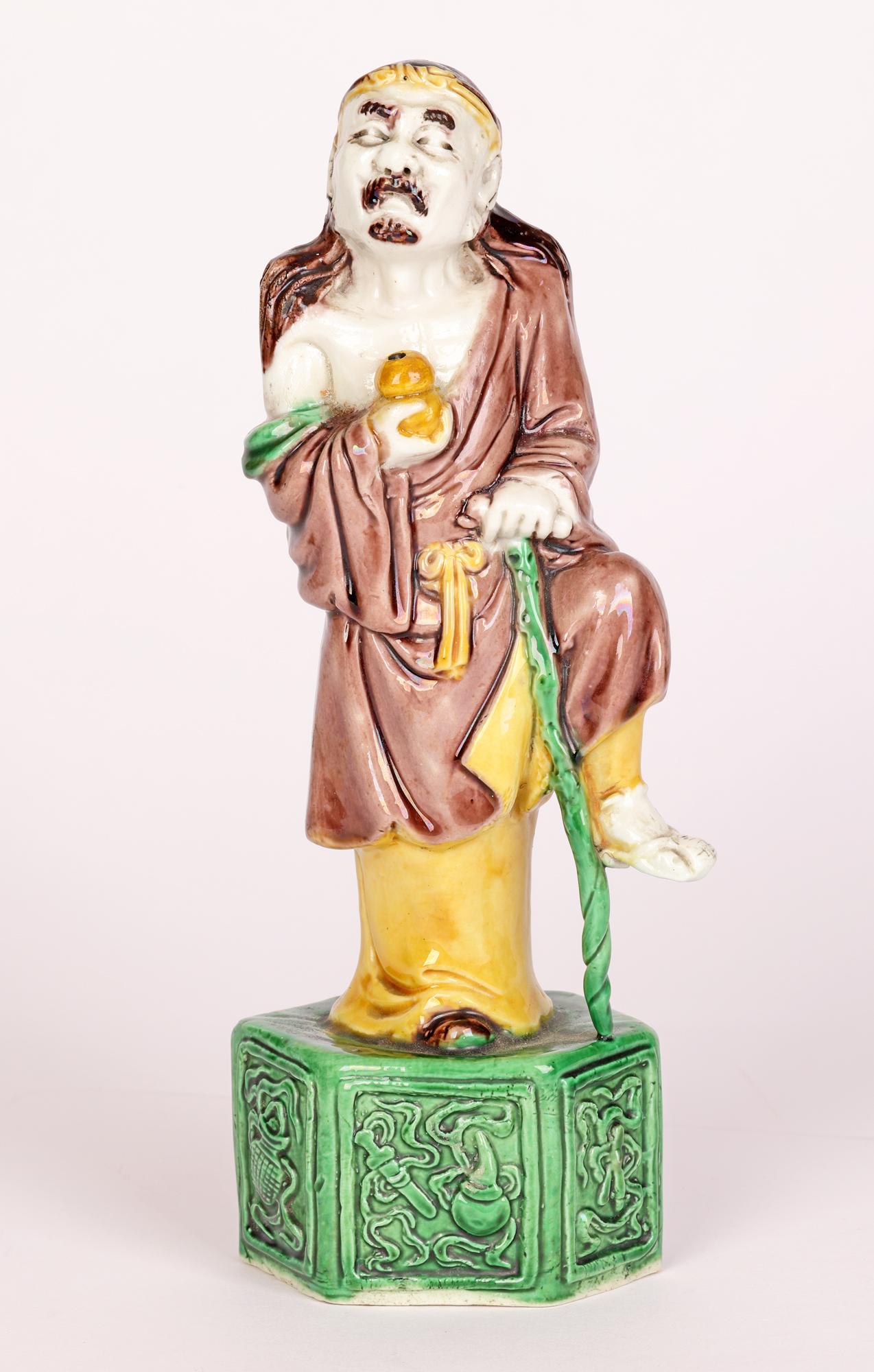 A fine antique Chinese porcelain figure of Immortal decorated in sancai glazes dating from 19th century. The figure stands raised on a six-sided pedestal base and is dressed in loosely fitting trousers and robe tied around the waist with his long
