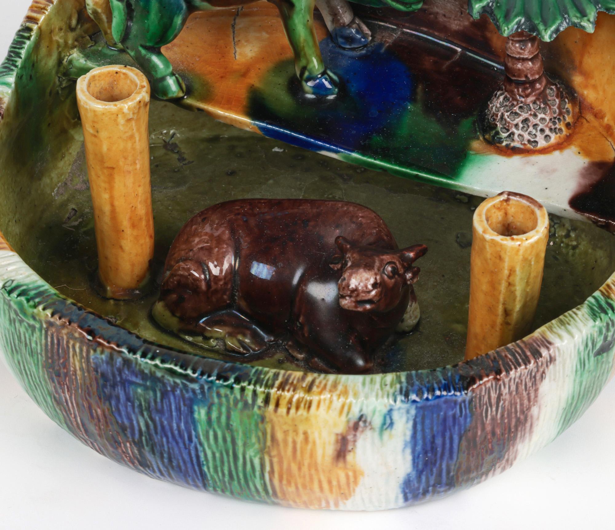 A stylish antique Chinese Qing sancai glazed porcelain joss stick holder formed as an oasis or pen with cows and palm tree dating from the early 19th century. The hand-crafted joss stick holder is of rounded shape with a raised and shaped edge