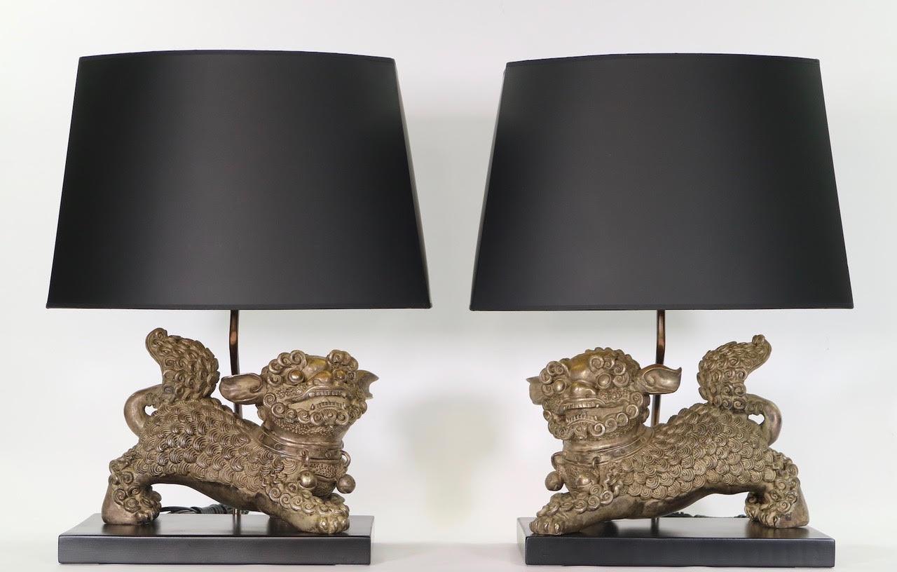 Chinese late Qing dynasty pair of table lamps with silver plated bronze foo dogs or foo dragons, mounted on ebonized wood bases. The sculptures have intricate metal carving and date from the early 20th century.
The pair is fully restored with all
