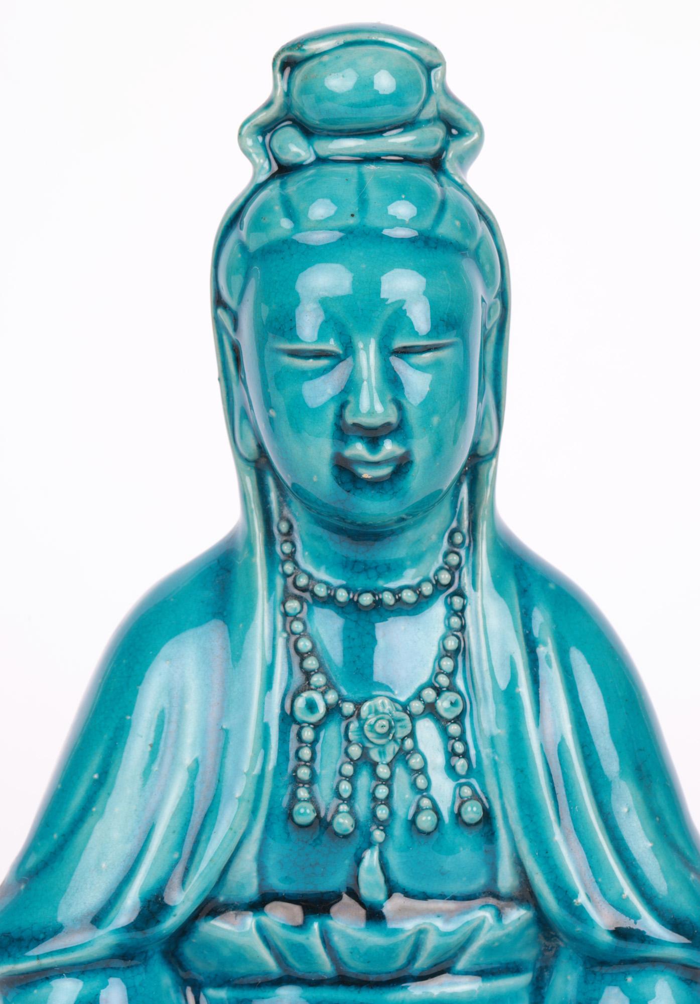 A very fine and attractive Chinese Qing Dynasty turquoise glazed figure of Guanyin dating from the 19th Century or possibly earlier. The hollow biscuit porcelain figurine sits cross legged raised on a lotus flower base and holds a pearl in her lap