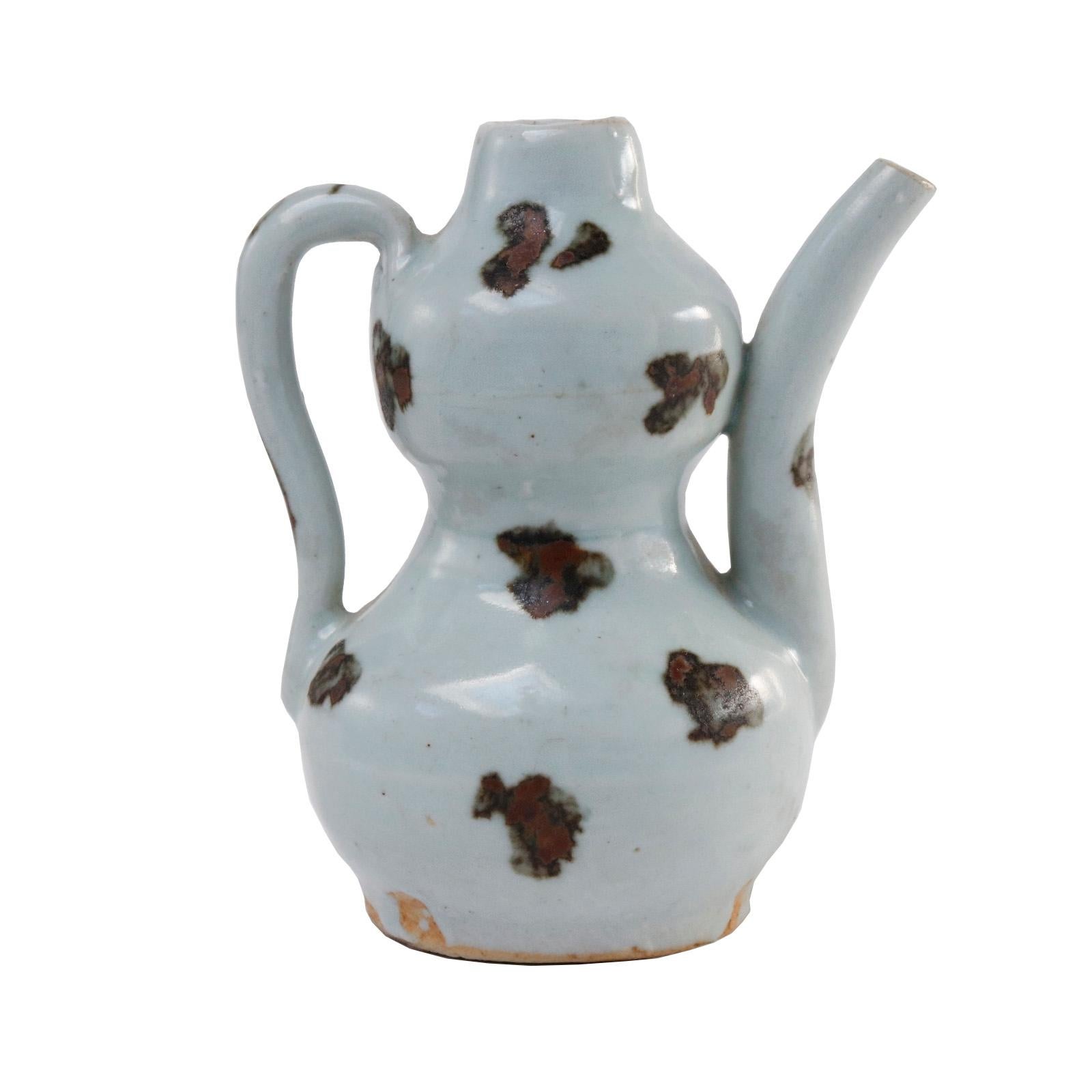 Chinese Qingbai gourd-shaped spotted ewer covered in an opaque milky bluish-white yingqing (shadow blue) glaze, bearing irregular patches of brown/black iron oxide, formed handle and arching spout, unglazed base, orange coloration to exposed