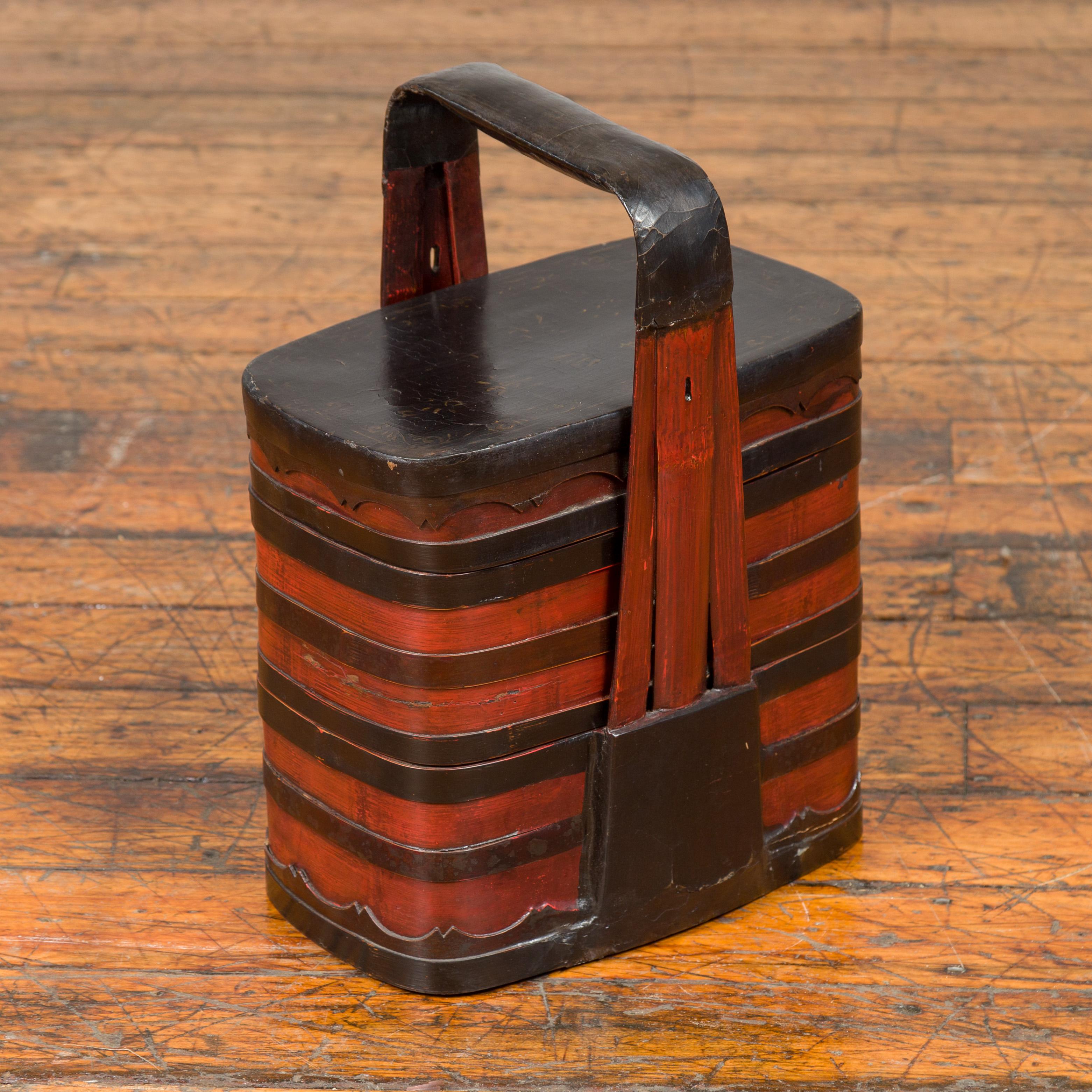 A Chinese antique red and black lacquered tiered lunch box from the early 20th century, with large handle and calligraphy. Crafted in China during the early years of the 20th century, this tiered lunch box features a black lid adorned with painted