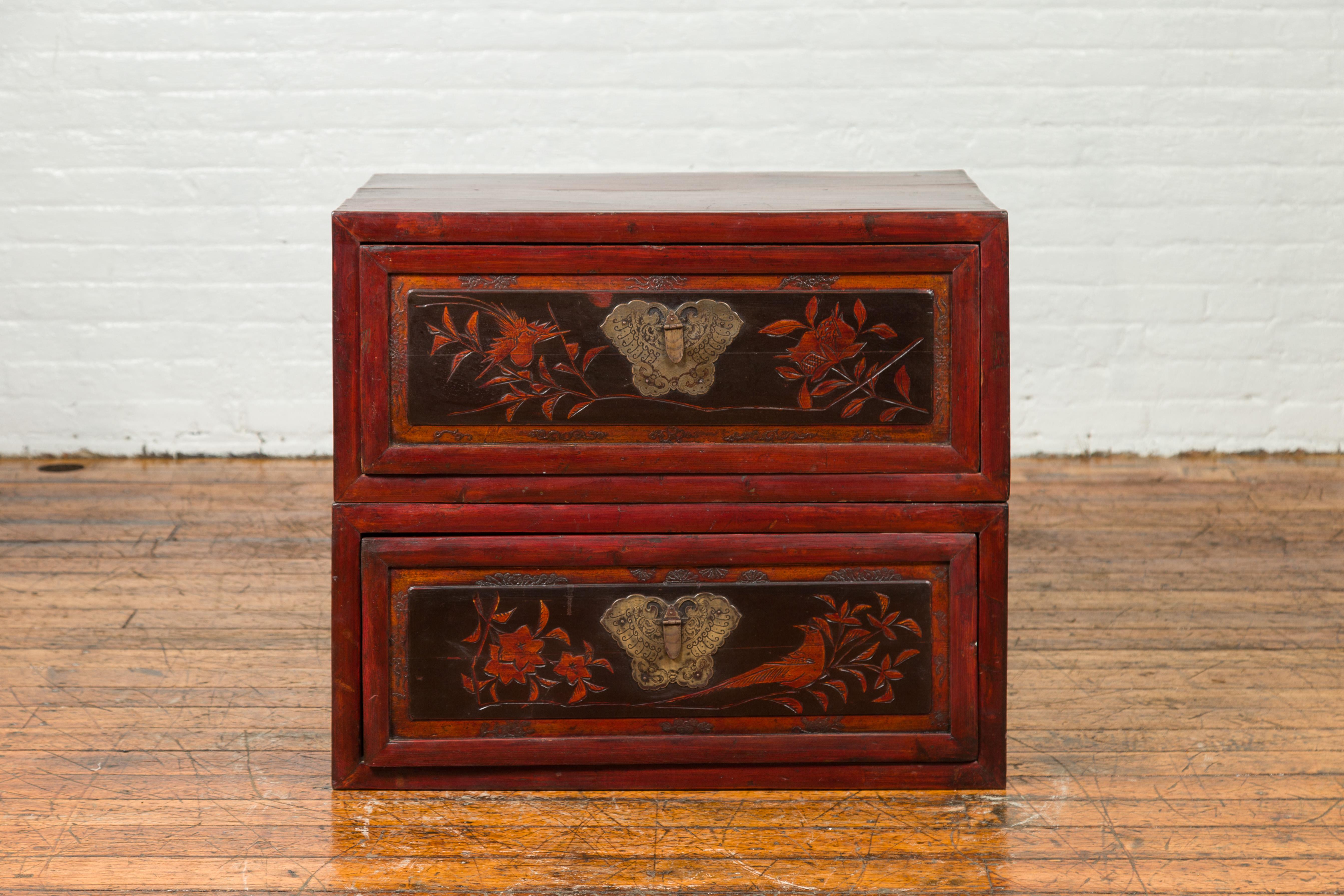An antique Chinese red and black lacquered two-part storage cabinet with butterfly bronze hardware and carved floral design. Crafted in China, this two-sectioned storage cabinet features a red lacquered body accented with black lacquer on the